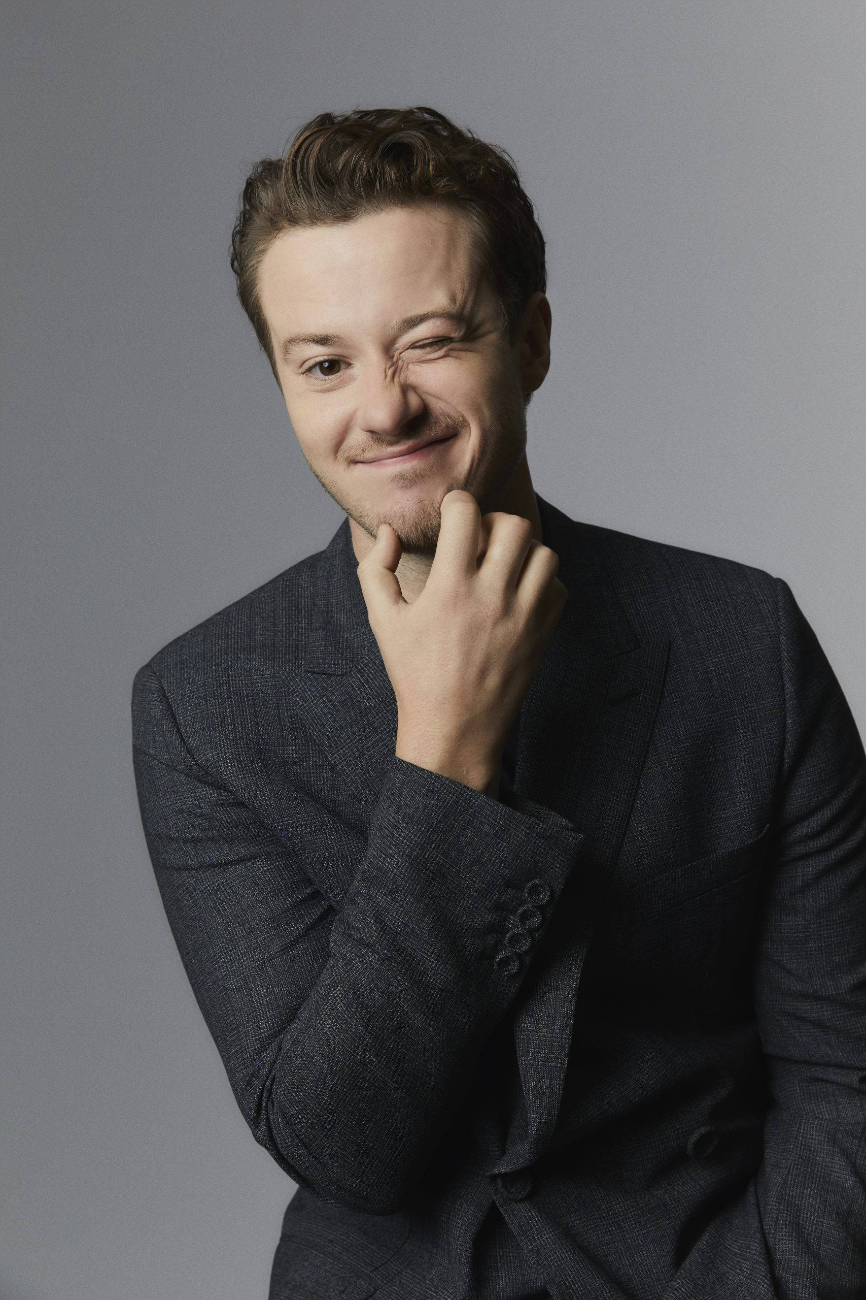 Celebrity 桌布 壁紙 — 一名身穿深色西裝的男子在純灰色背景前，將下巴擱在手上，露出溫暖的笑容。