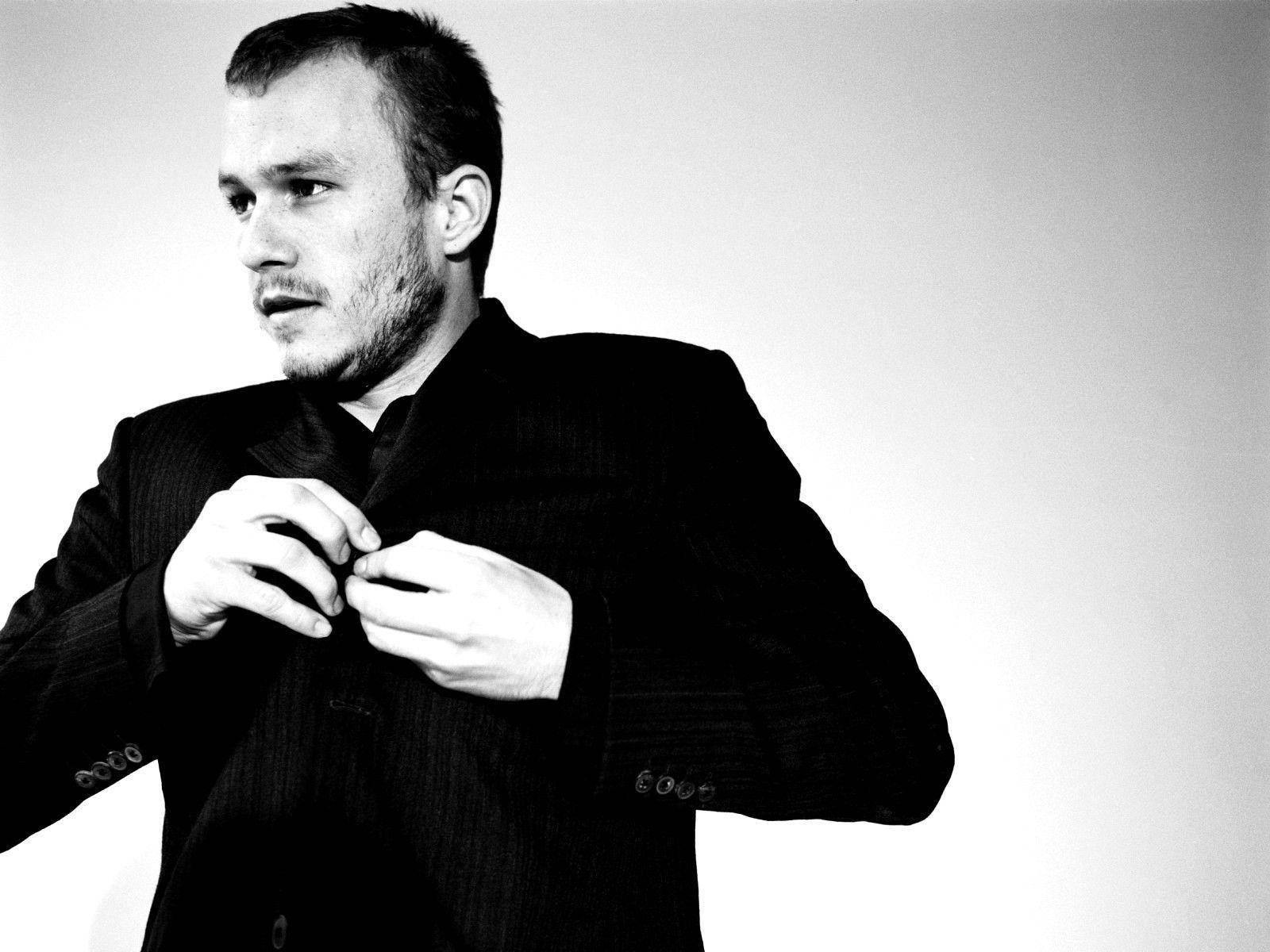 Heath Ledger 桌布 壁紙 — 一名身穿深色西裝的男子在純白背景下扣上外套鈕扣的黑白肖像。