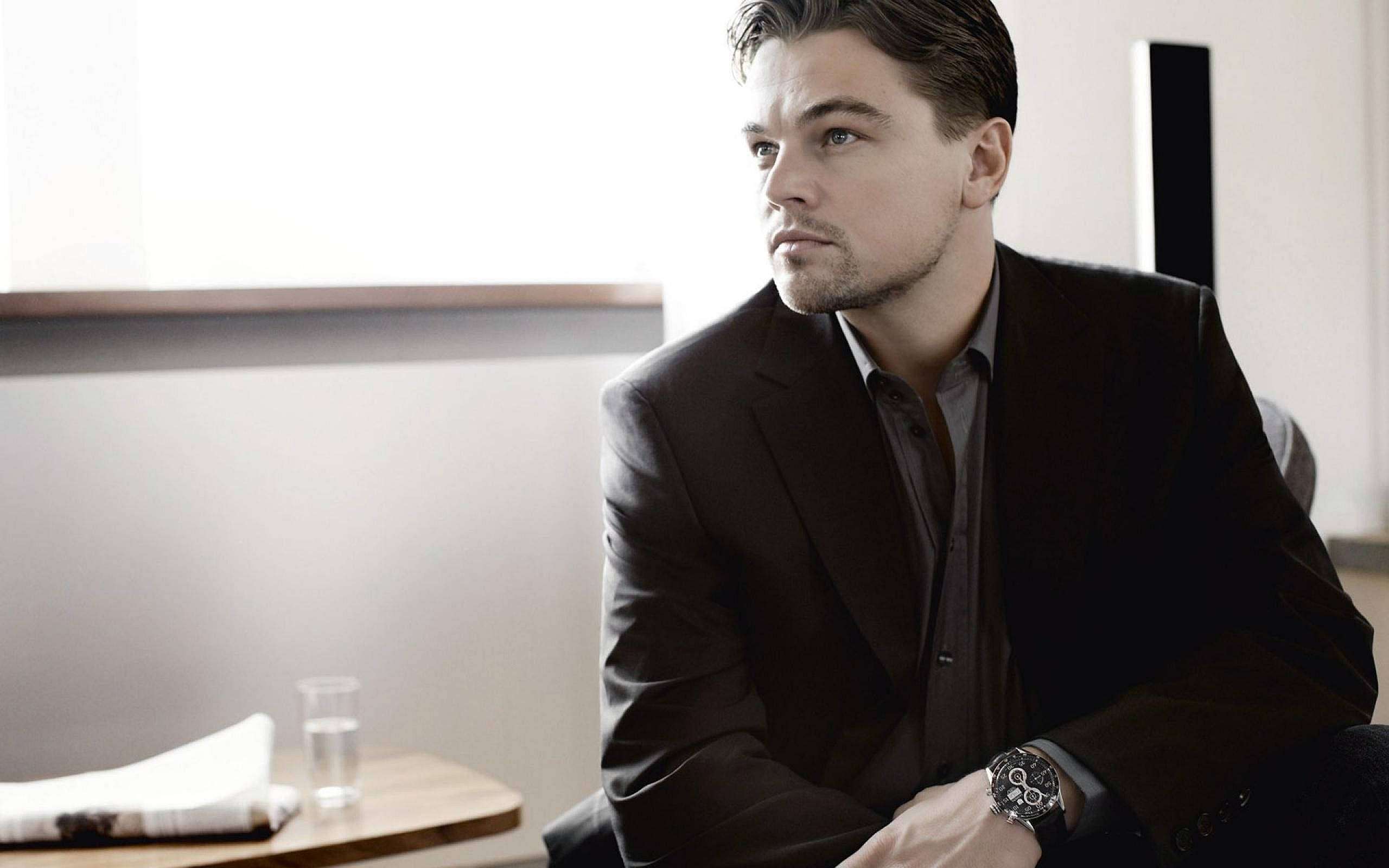 Dicaprio 桌布 壁紙 — 一名身穿深色西裝的男子坐在窗邊沉思，柔和自然光凸顯他若有所思的表情。