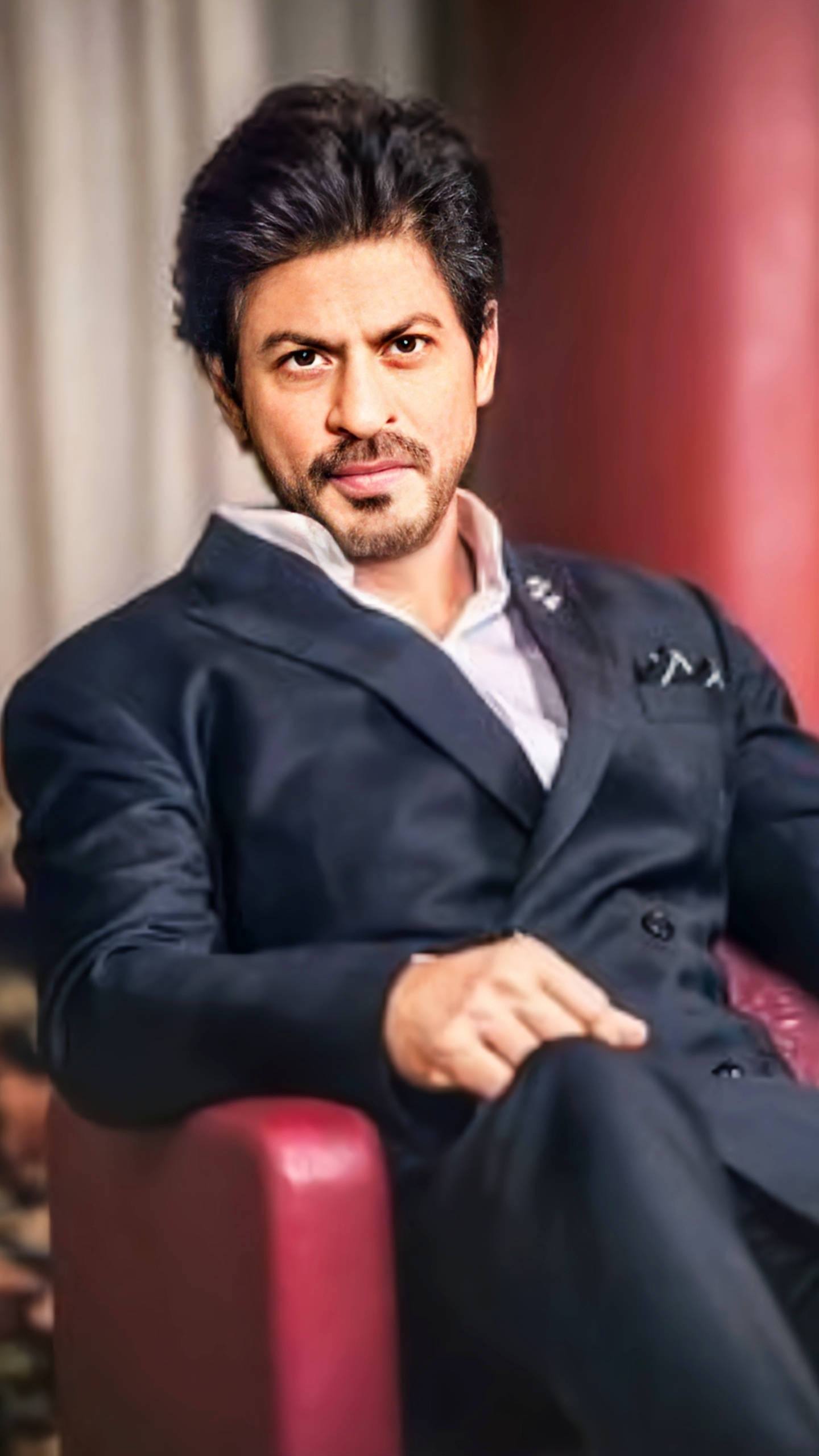 Shahrukh 桌布 壁紙 — 一名身穿深色西裝的男子自信地坐在紅色椅子上，表情嚴肅，背景模糊。