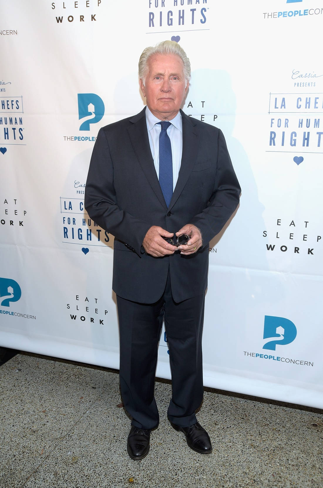 actor 桌布 壁紙 — 一名身穿深色西裝的男子自信地站在一個有品牌背景的慈善活動中。