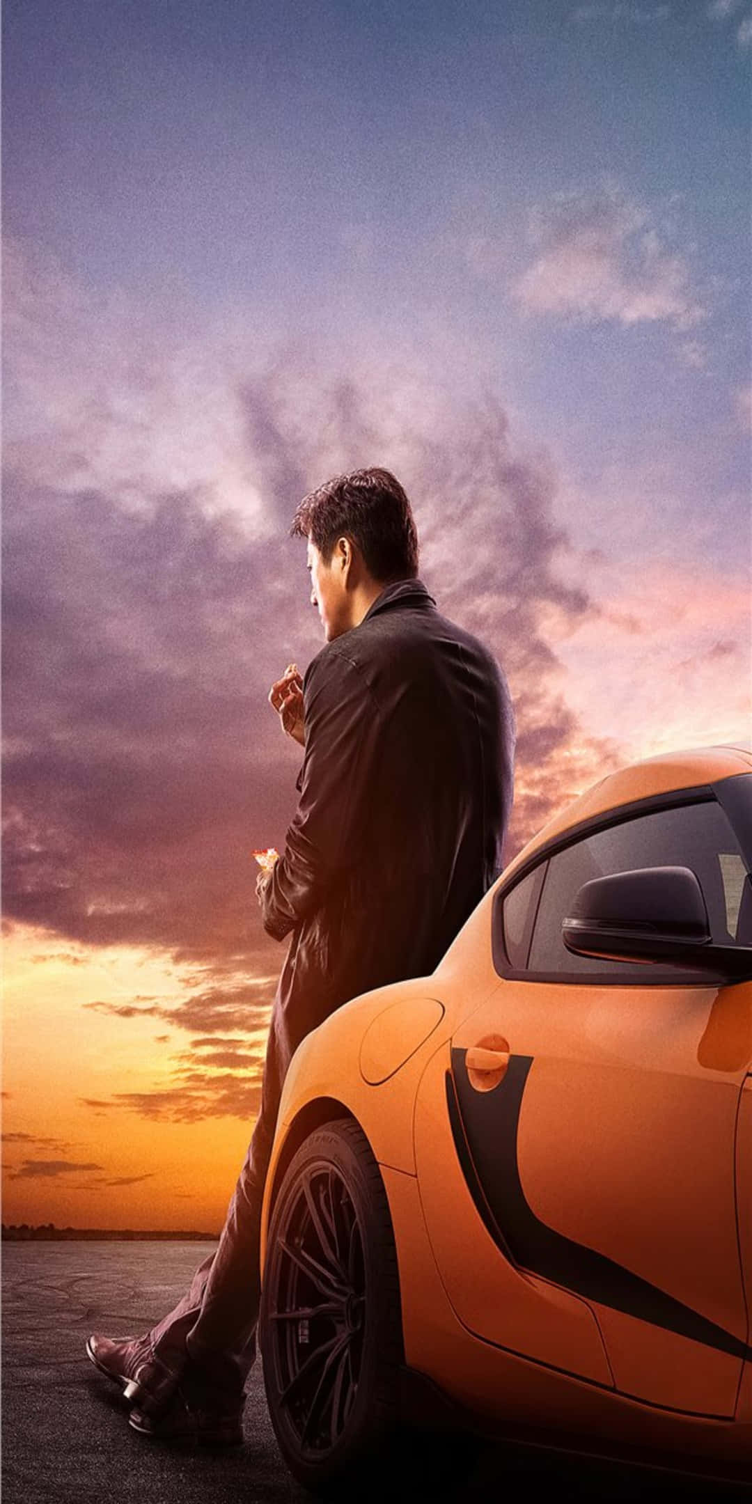 Pixel 3 Fast And Furious 桌布 壁紙 — 一名身穿深色西裝的男子靠在一輛充滿活力的橙色跑車旁，背景是帶有紫色和金色雲彩的戲劇性日落天空。