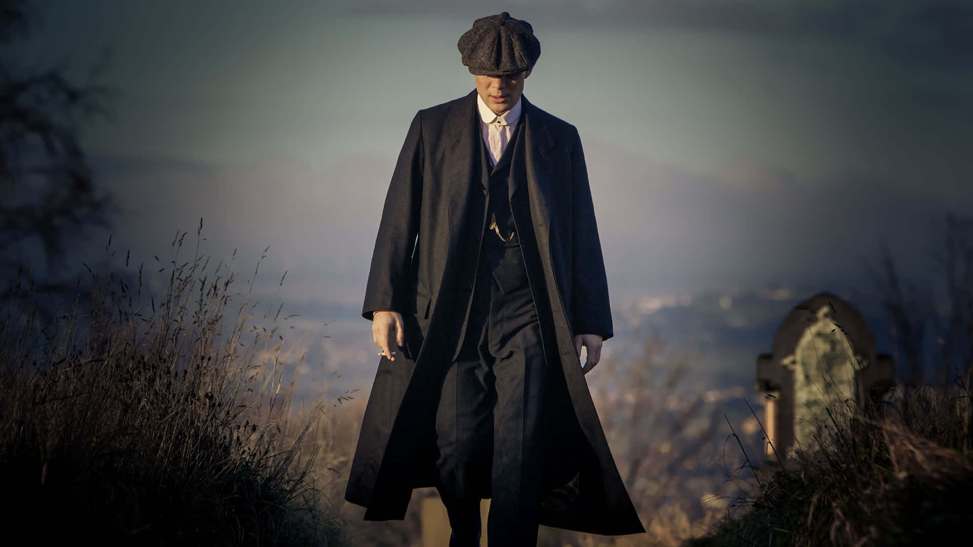 身穿風衣和扁帽的男子在黃昏時走過霧氣瀰漫的墓地。 — Peaky Blinders 壁紙