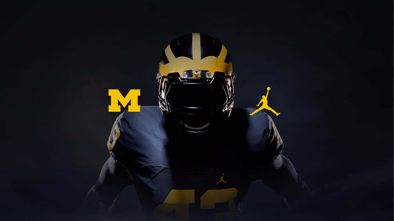 Michigan Football 桌布 壁紙 — 一名身穿深藍色和金色球衣、戴著頭盔的美式足球運動員站在黑色背景前，兩側有黃色的M和Jordan標誌。