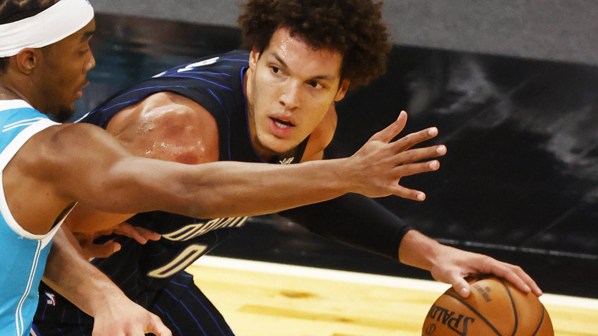 aaron gordon 桌布 壁紙 — 一名身穿深藍色球衣的籃球運動員在硬木地板上運球，同時被一名身穿淺藍色球衣的對手緊密防守。