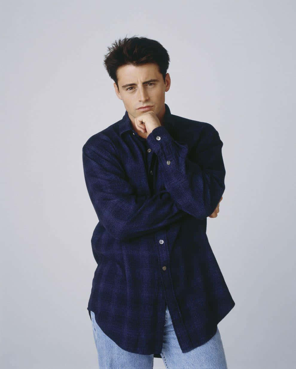 Matt Leblanc 桌布 壁紙 — 一名身穿深藍色鈕扣襯衫和牛仔褲的男子，在純灰色背景前，手托下巴，若有所思地擺姿勢。