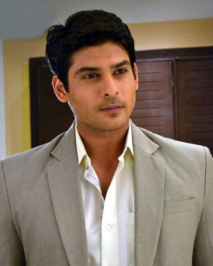 Sidharth Shukla 桌布 壁紙 — 一名身穿淺灰色西裝和白色襯衫的男子，在室內以嚴肅的表情站在木門背景前。