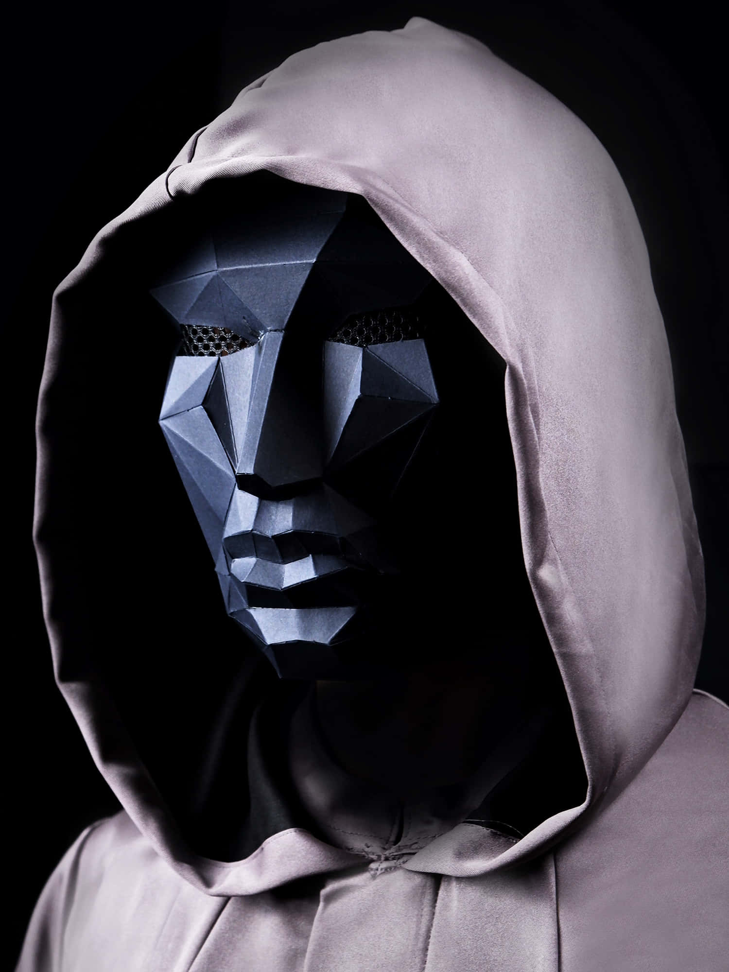 Mask 桌布 壁紙 — 一名身穿淺灰色連帽衫的人，在黑色背景前戴著深色幾何金屬面具。