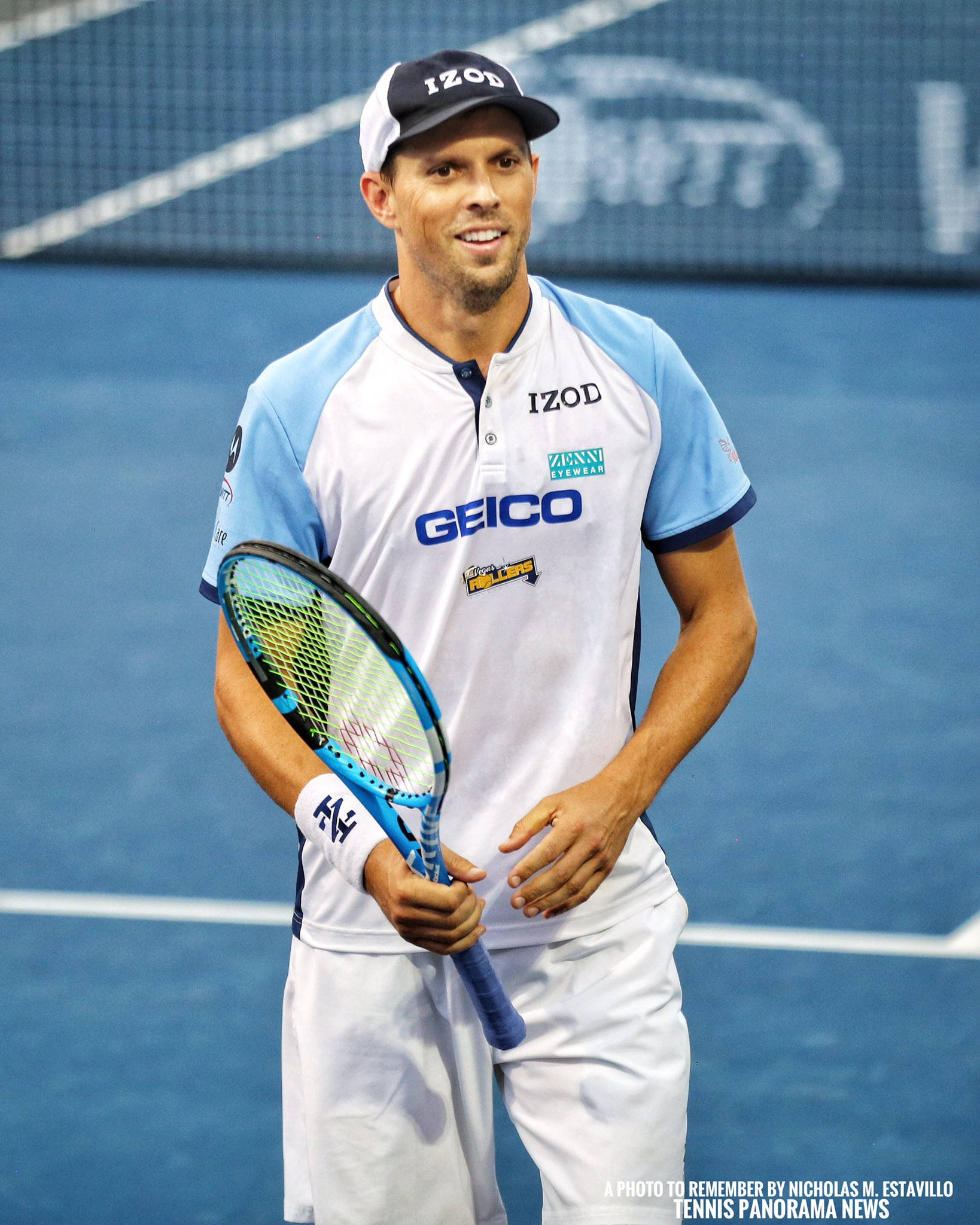 Tennis 桌布 壁紙 — 一名身穿淺藍色和白色Izod襯衫的男性網球運動員在藍色硬地球場上微笑著手持球拍。
