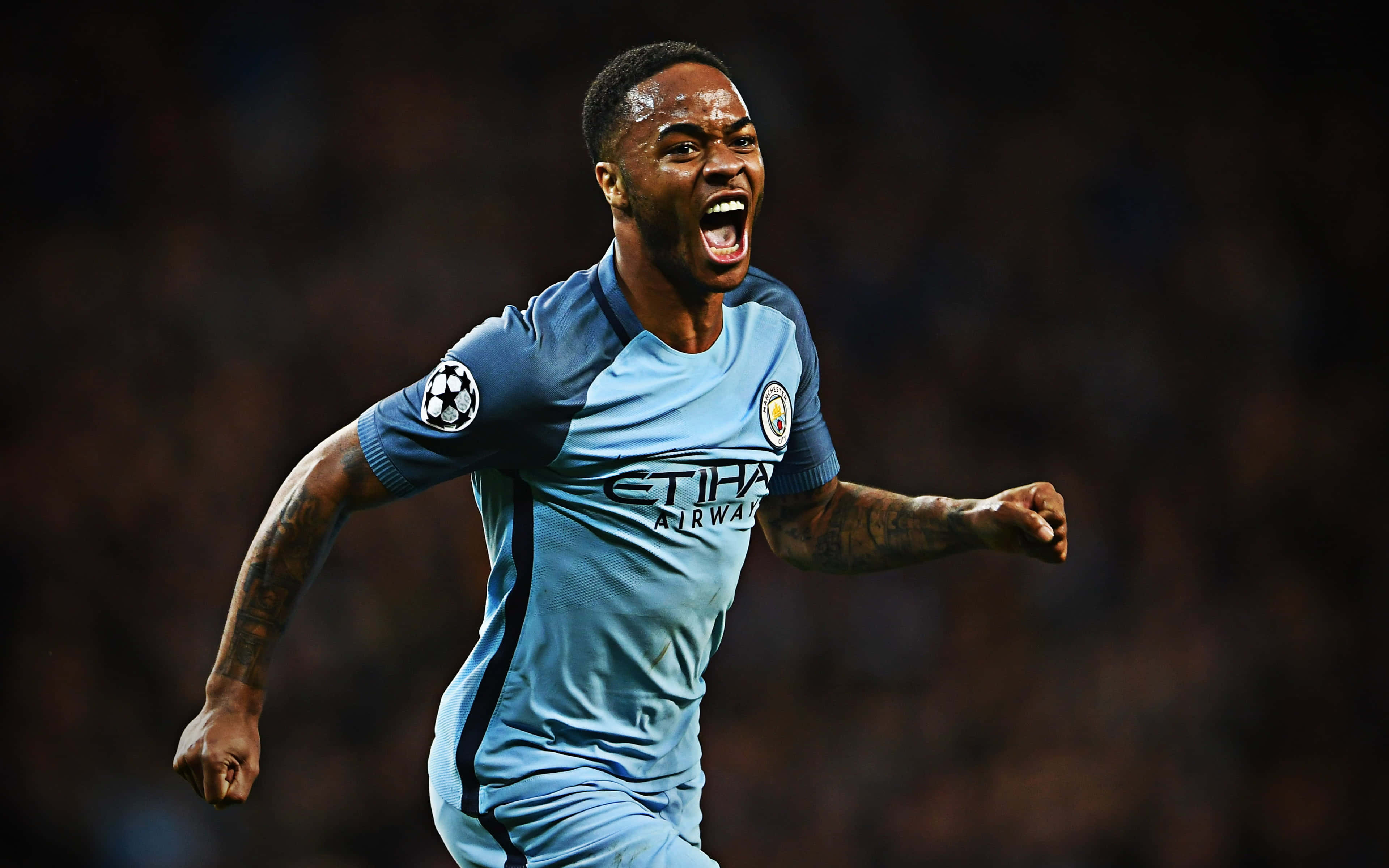Sterling 桌布 壁紙 — 一名身穿淺藍色曼城球衣的足球員在夜間球場張開雙臂、張開嘴巴慶祝。