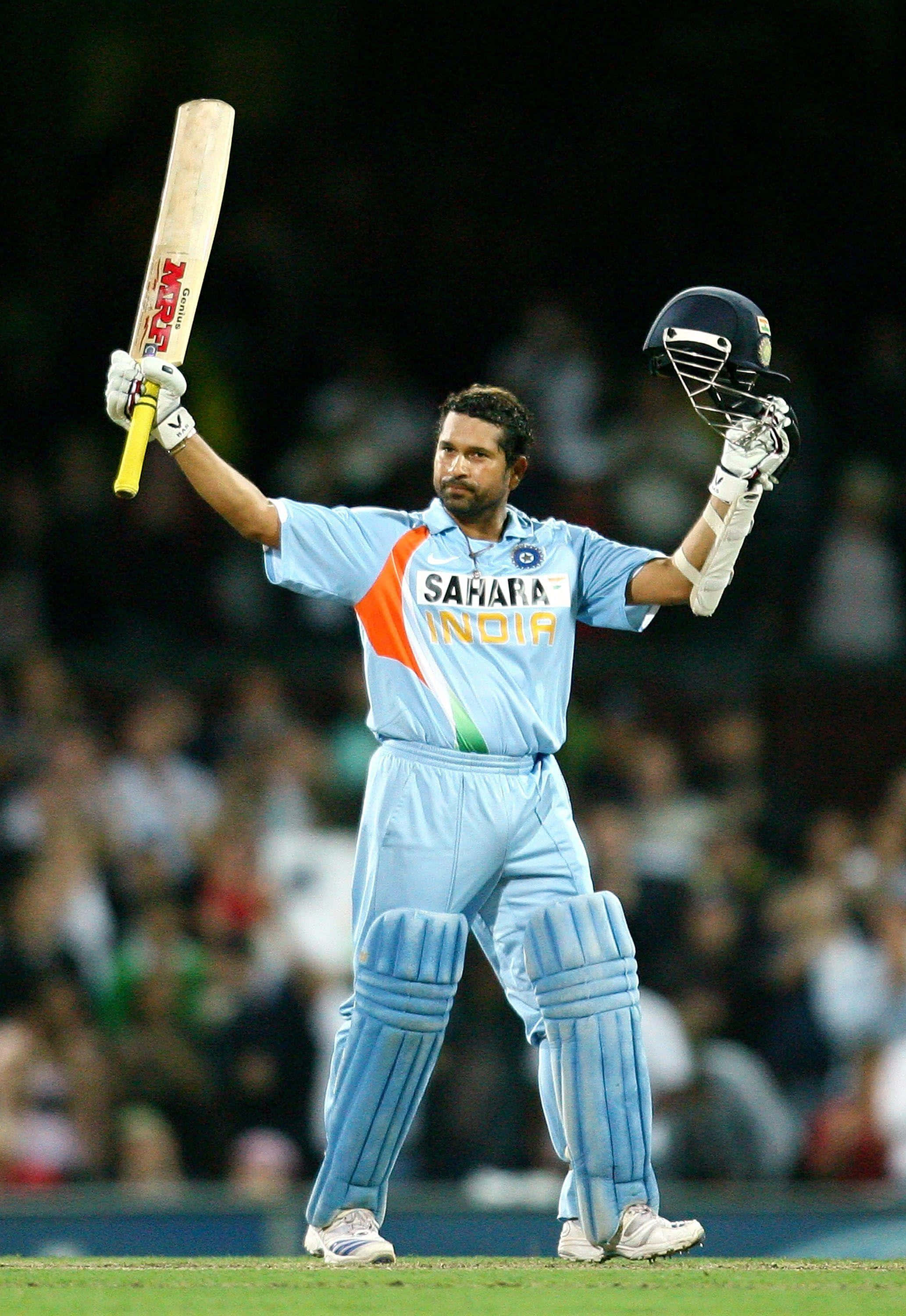 Sachin Tendulkar 桌布 壁紙 — 一名身穿淺藍色球衣的板球運動員在球場燈光下高舉球棒和頭盔，擺出勝利姿勢。