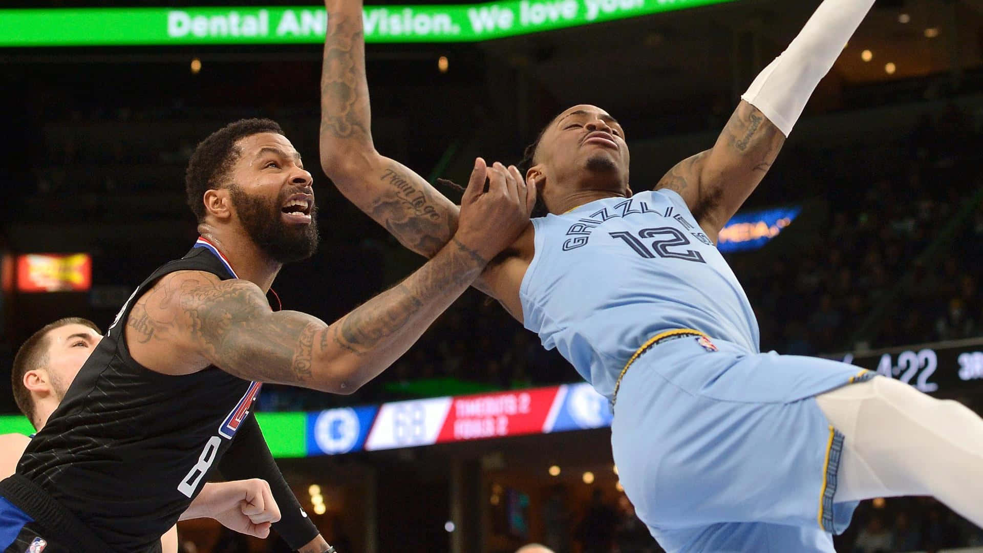NBA 桌布 壁紙 — 一名身穿淺藍色球衣的籃球運動員在場館燈光下，被身穿黑色球衣的對手緊密防守，動態地跳起投籃。