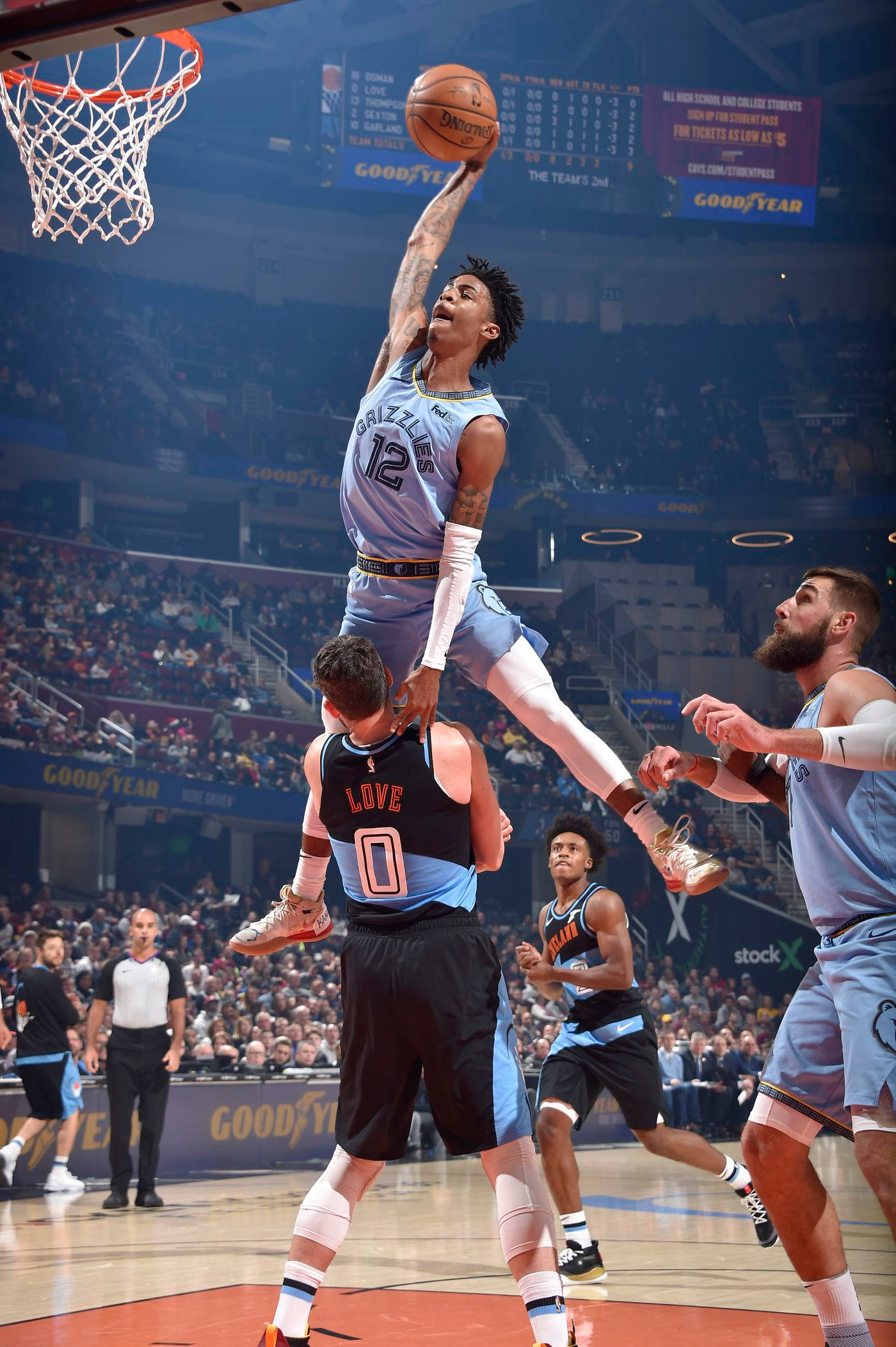 Grizzlies 桌布 壁紙 — 一名身穿淺藍色球衣的籃球運動員在擠滿觀眾的場館中高高躍起灌籃，防守球員在下方觀望。