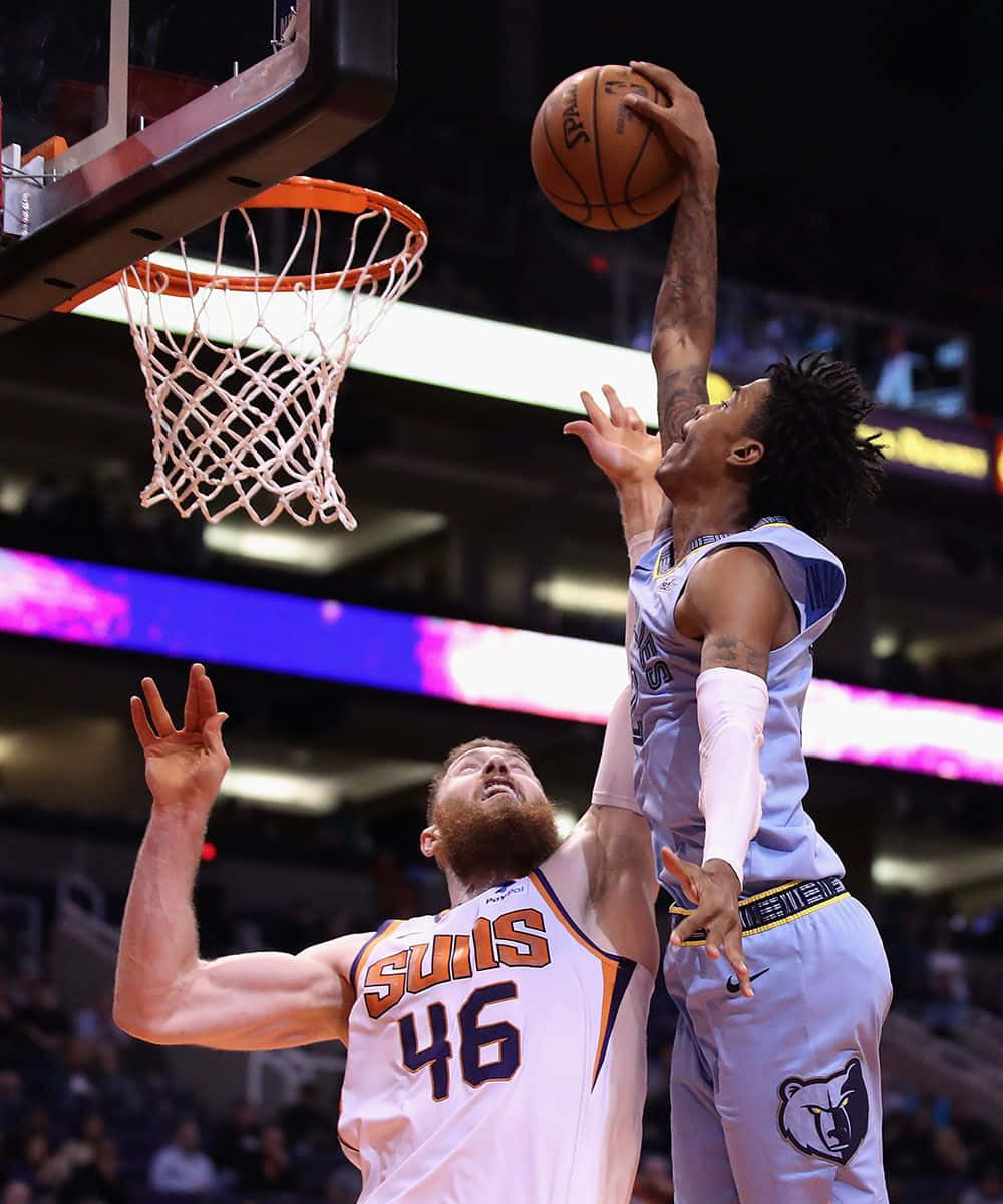 Ja Morrant 桌布 壁紙 — 一名身穿淺藍色球衣的籃球運動員跳向籃框，同時被一名身穿白色Suns球衣、留鬍子的球員防守。