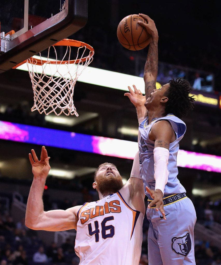 Ja Morant 灌籃 桌布 壁紙 — 一名身穿淺藍色球衣的籃球運動員跳起灌籃，而一名身穿白色Suns球衣的防守球員試圖封阻。