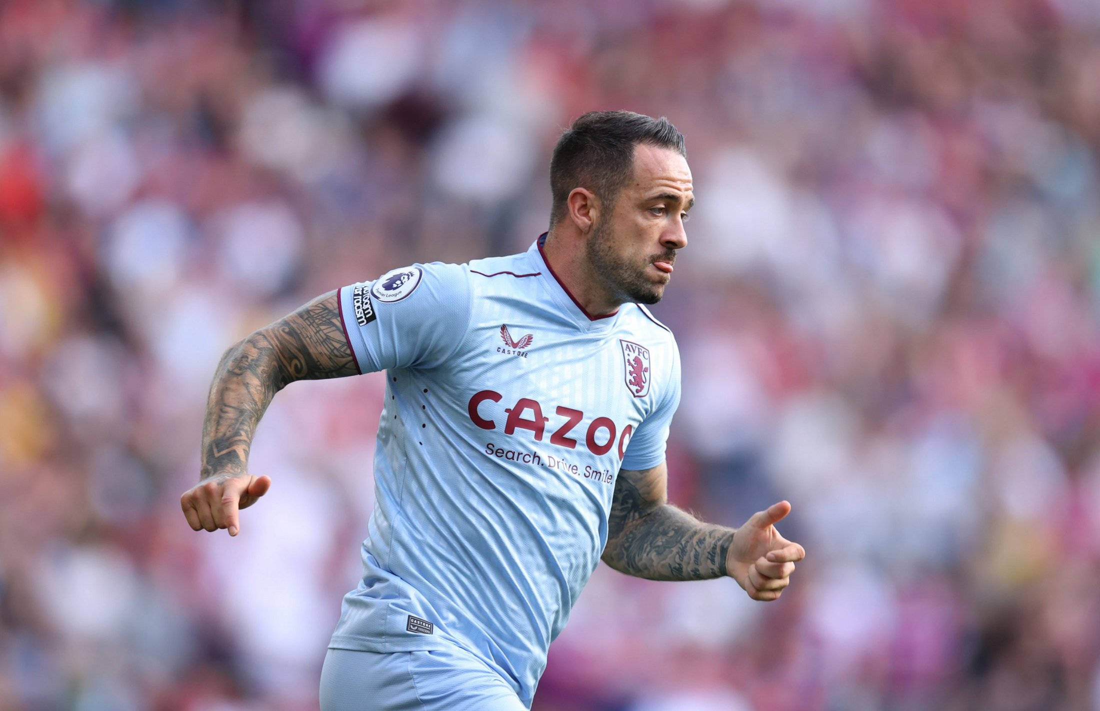 Aston Villa 桌布 壁紙 — 一名身穿淺藍色球衣的足球員，在模糊的體育場人群背景下，專注地向前衝刺。