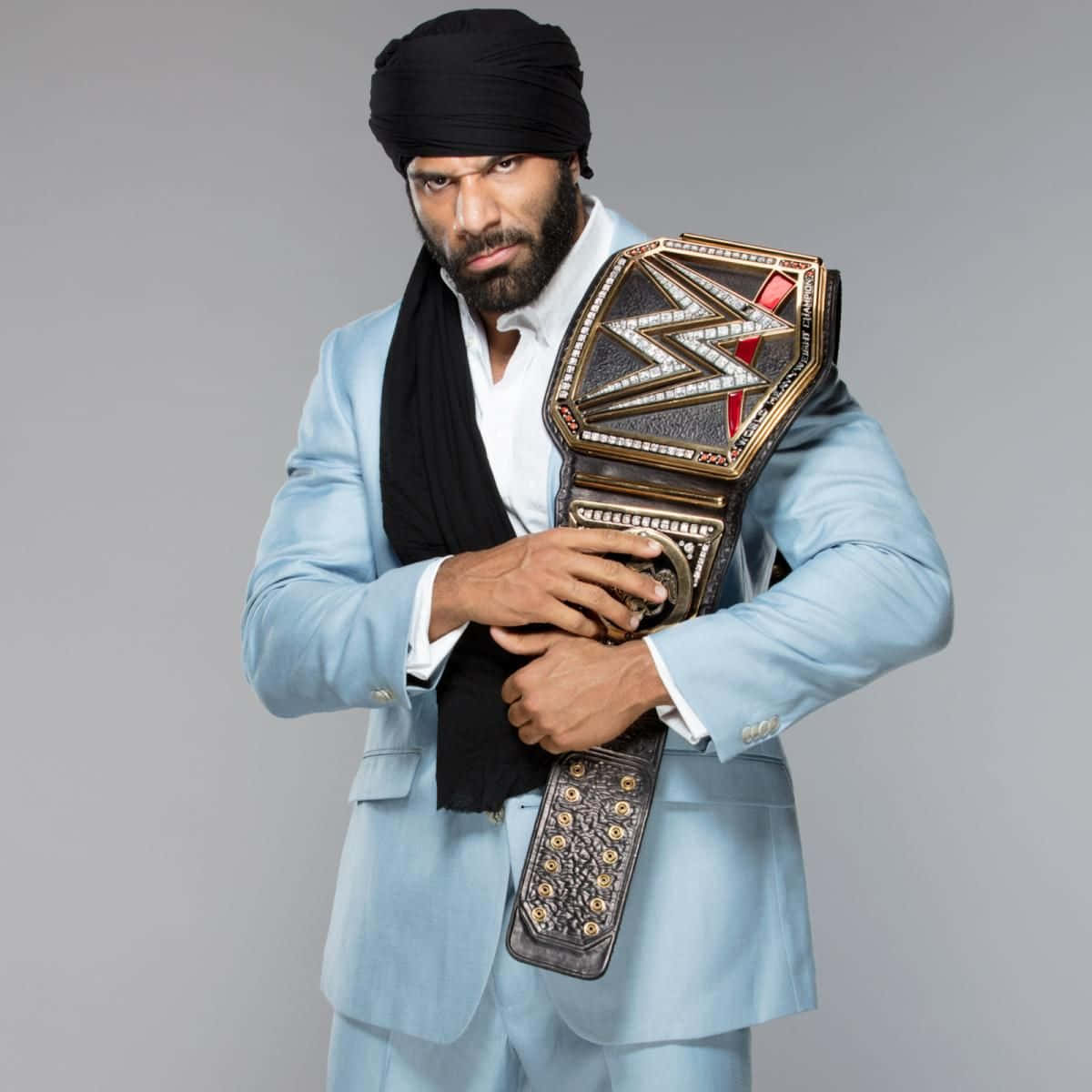 WWE 桌布 壁紙 — 一名身穿淺藍色西裝和黑色頭巾的男子，在灰色背景下以嚴肅的目光手持WWE冠軍腰帶。