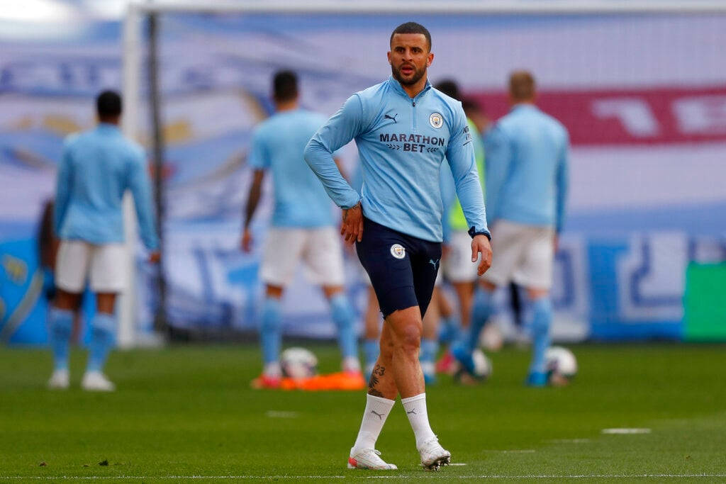 Kyle Walker 桌布 壁紙 — 一名身穿淺藍色訓練裝備的足球運動員走過綠色球場，背景中的隊友模糊不清。