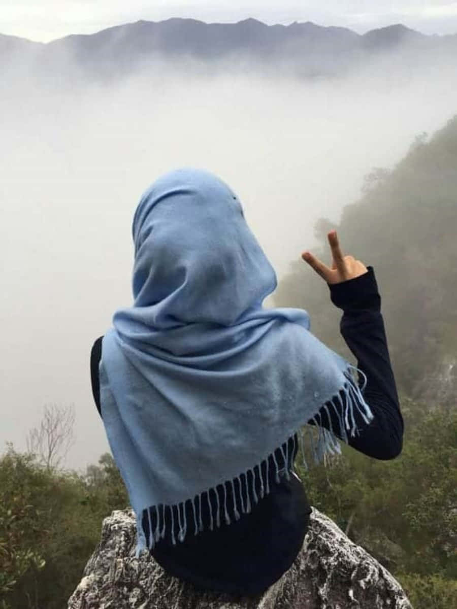 muslim 桌布 壁紙 — 一名身穿淺藍色頭巾的人坐在岩石懸崖上，俯瞰霧氣瀰漫的山谷，做出和平手勢。