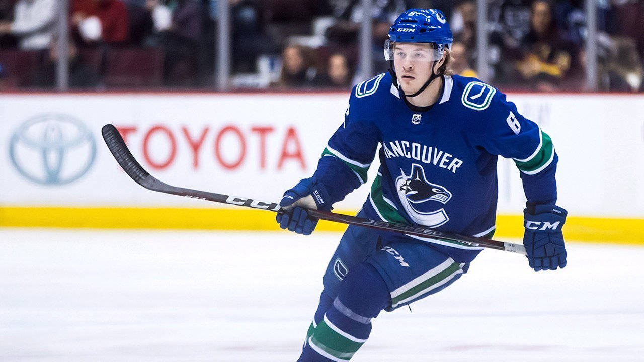 運動 桌布 壁紙 — 一名身穿溫哥華加人隊（Vancouver Canucks）藍色球衣的冰上曲棍球運動員，手持球桿在冰上激烈滑行。