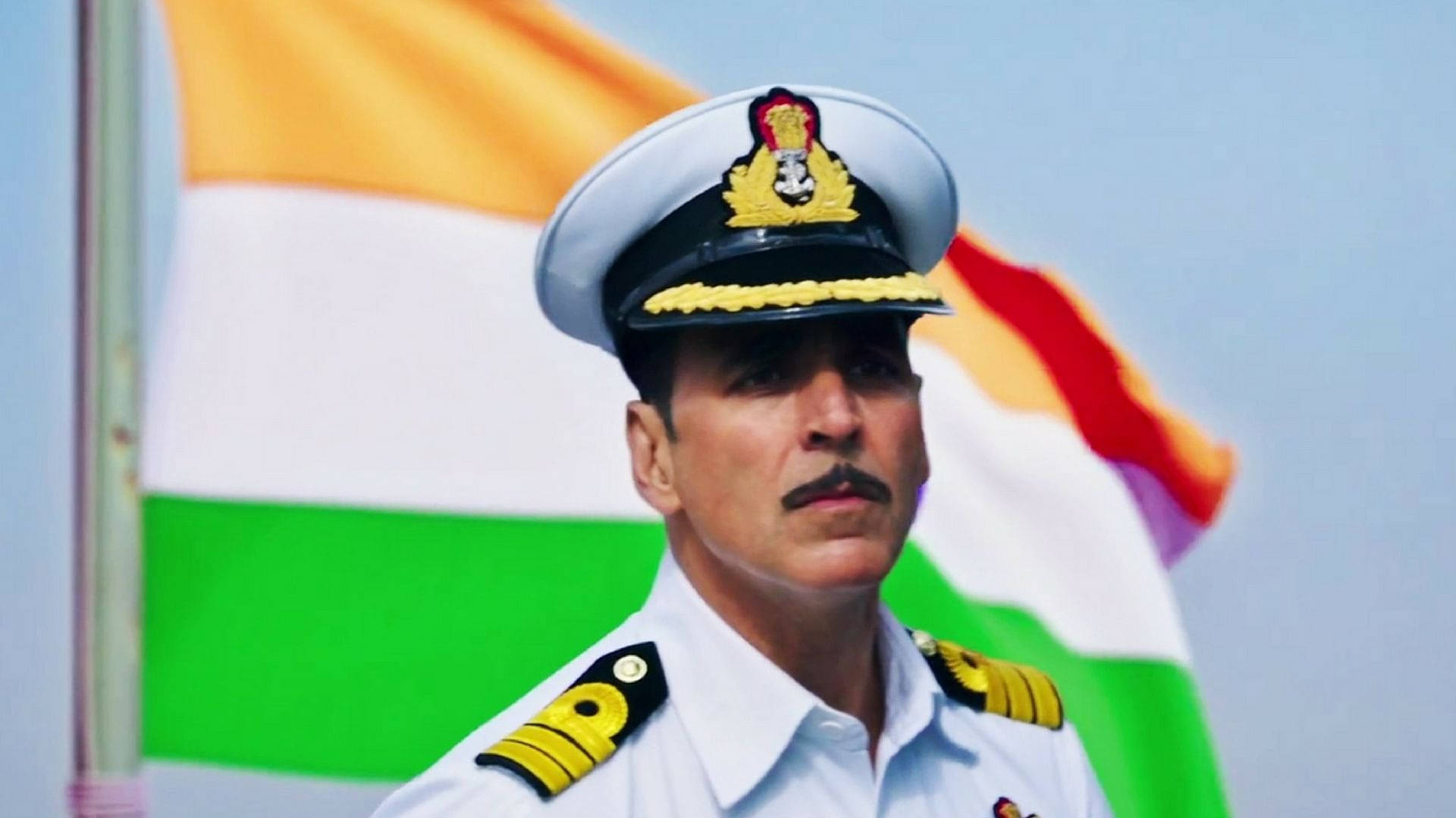 Akshay Kumar 桌布 壁紙 — 一名身穿潔白制服的海軍軍官，在晴朗藍天下莊嚴地站在飄揚的印度國旗前。