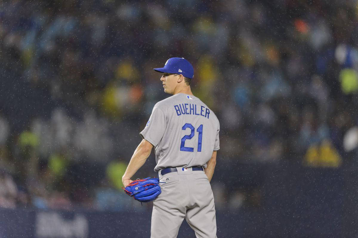 walker buehler 桌布 壁紙 — 一名身穿灰色制服、藍色21號的棒球投手在雨中離開，背景是夜間比賽的球場燈光。