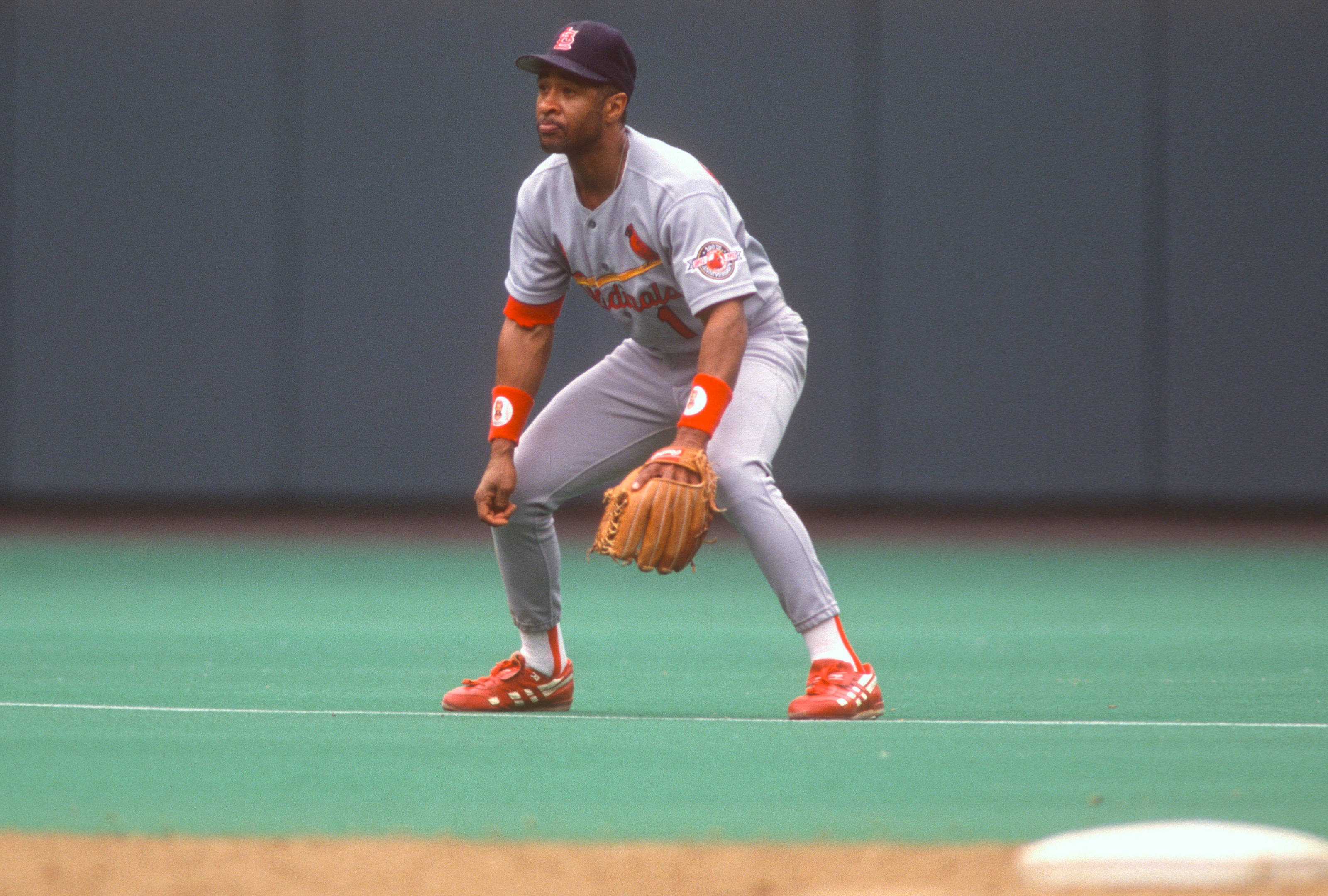 Ozzie Smith 桌布 壁紙 — 一名身穿灰色和橙色球衣的棒球選手在綠色場地上警覺地蹲下，準備接球。
