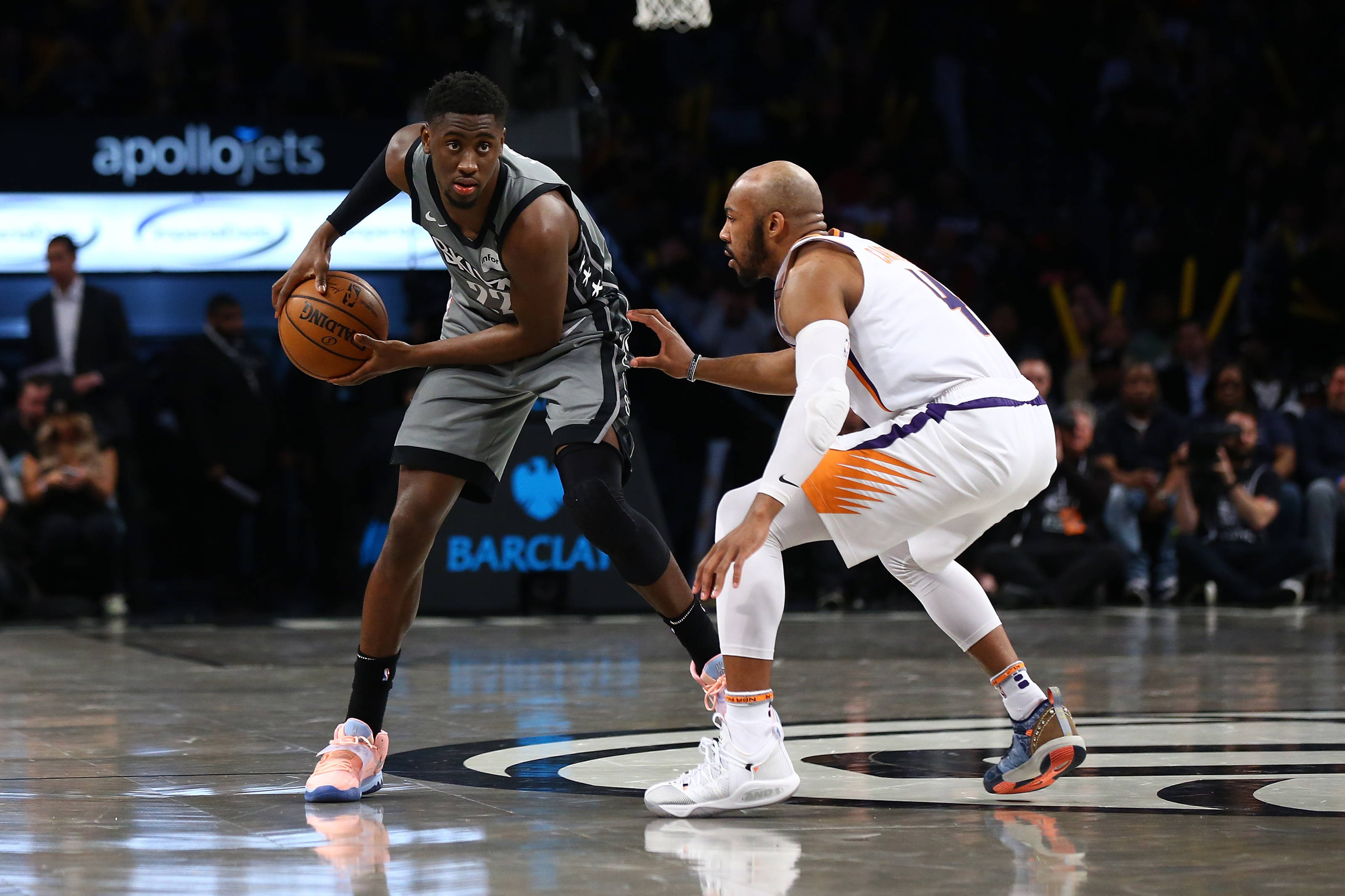 caris levert 桌布 壁紙 — 一名身穿灰色球衣的籃球運動員在拋光球場上運球，同時被一名身穿白色球衣的防守球員緊密防守。