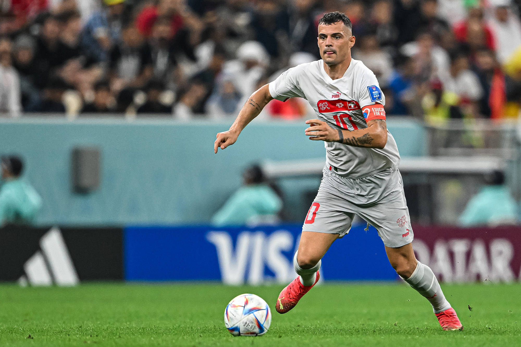 Football Players 桌布 壁紙 — 一名身穿灰色球衣的足球運動員在體育場燈光下，於充滿活力的綠色球場上運球，背景有模糊的觀眾。