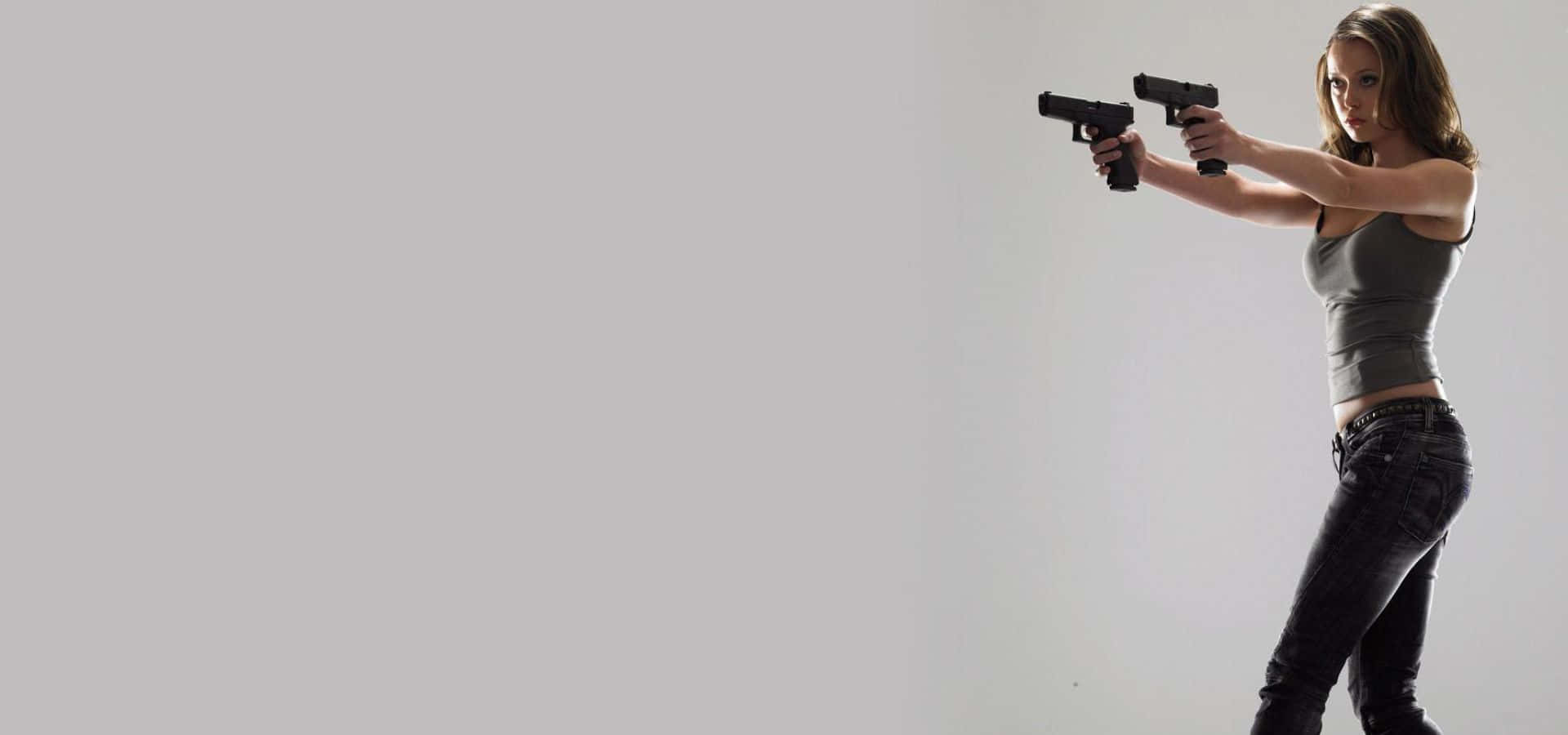 Shooting 桌布 壁紙 — 一名身穿灰色背心和牛仔褲的女子，在純白背景下全神貫注地瞄準兩把黑色手槍。