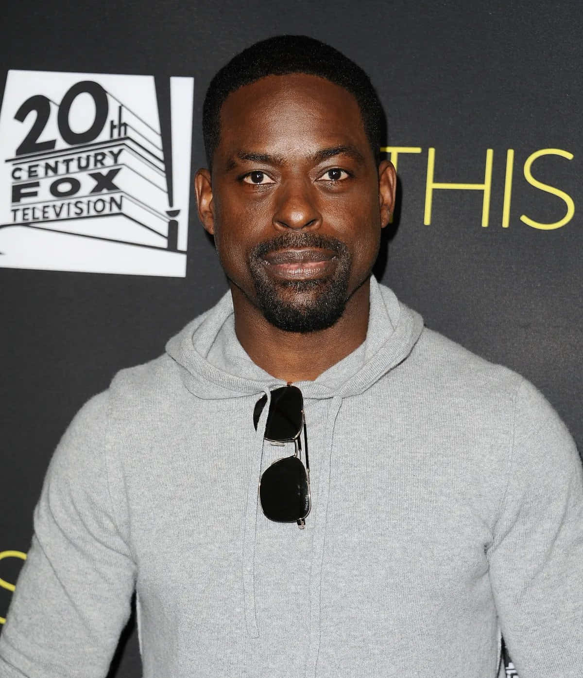 Sterling K Brown 桌布 壁紙 — 一名身穿灰色連帽衫、太陽眼鏡掛在領口的男子站在20th Century Fox Television的背景前。