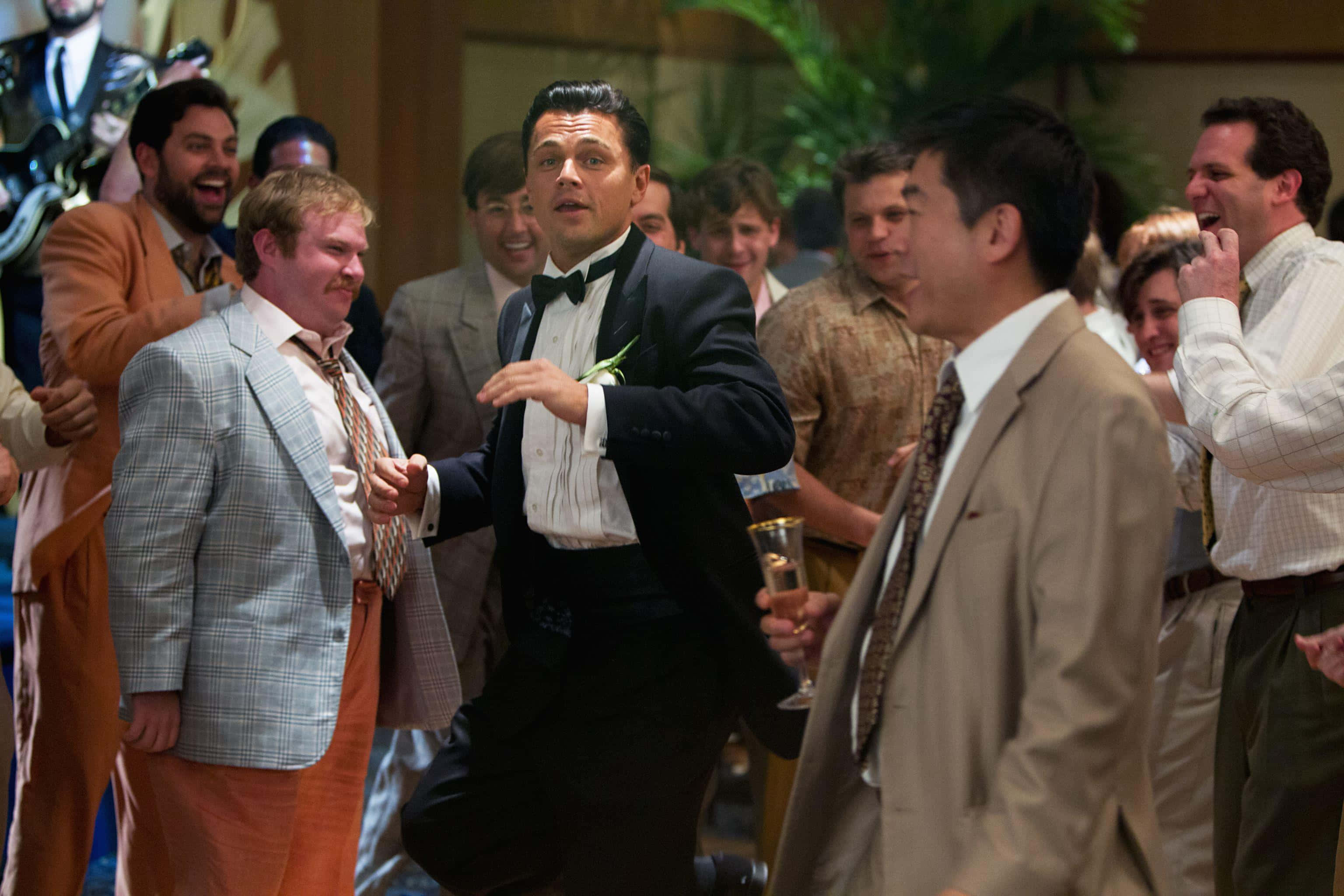 Wolf Of Wall Street 桌布 壁紙 — 一名身穿燕尾服的男士在擁擠的室內派對中充滿活力地跳舞，客人們笑著觀看。