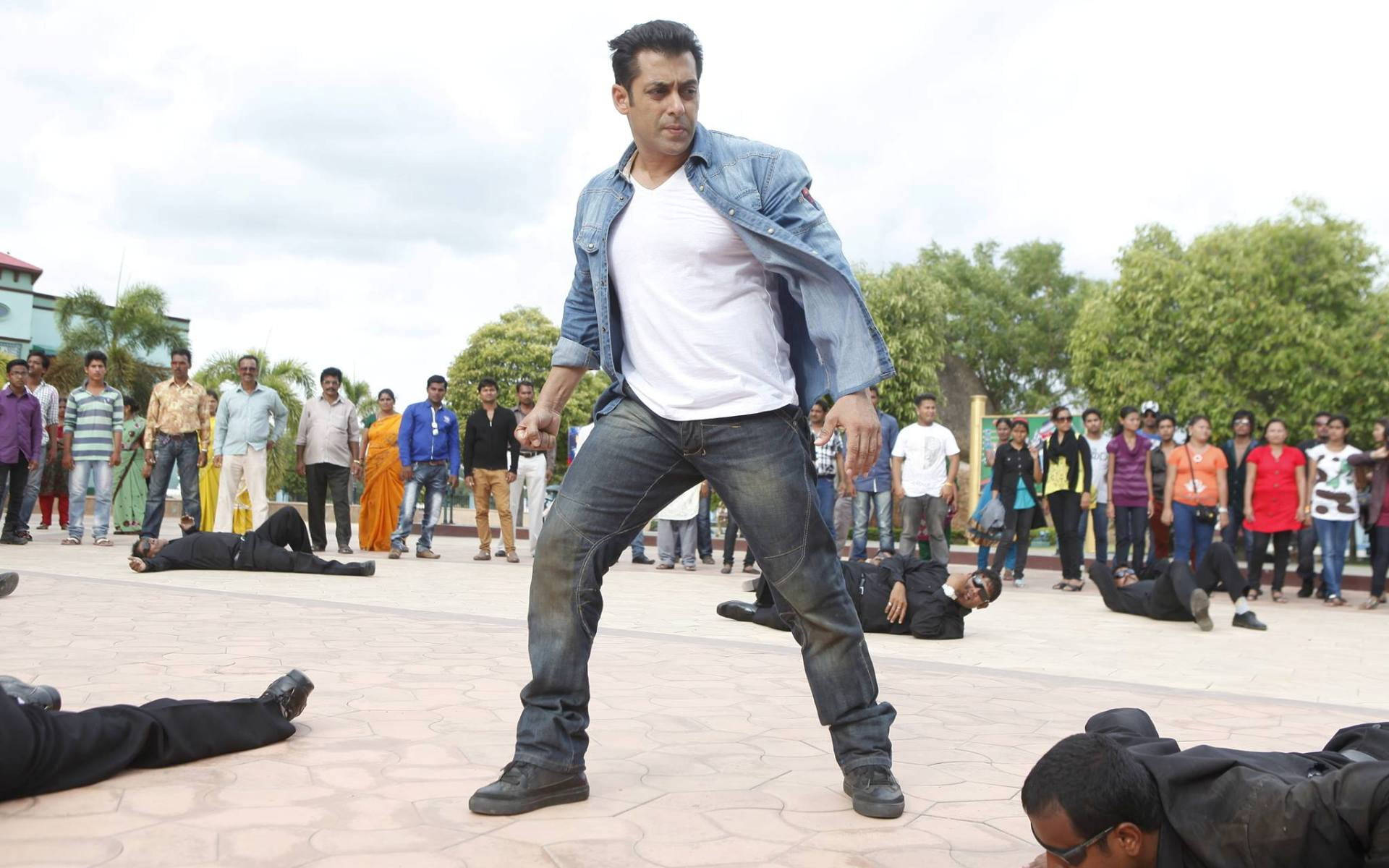 Salman Khan 桌布 壁紙 — 一名身穿牛仔外套的男子在戶外廣場上勝利地站在倒下的對手之上，旁觀者觀看。