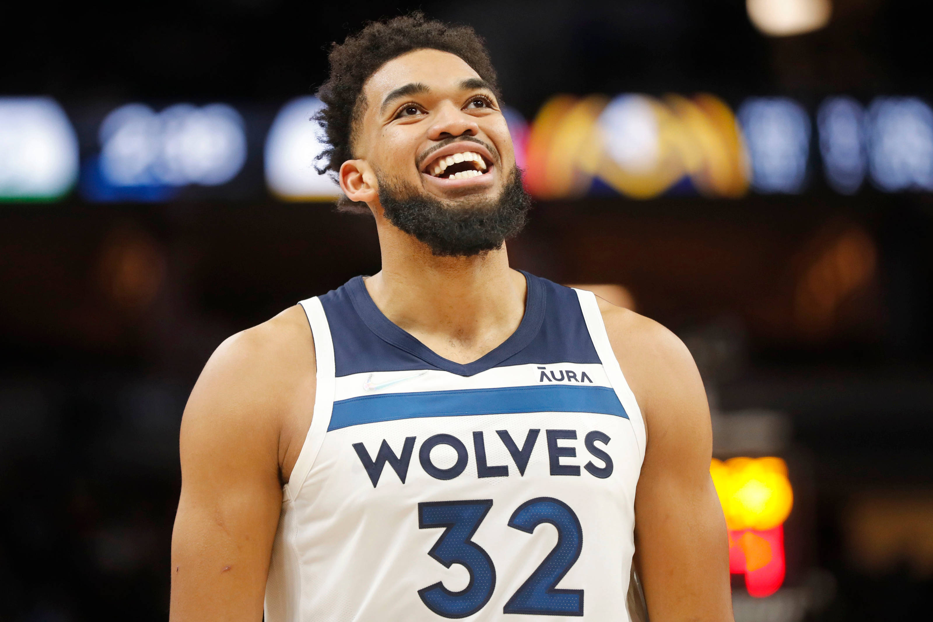 Timberwolves 桌布 壁紙 — 一名身穿狼隊球衣的籃球運動員在明亮的場館燈光下於比賽中開懷大笑。