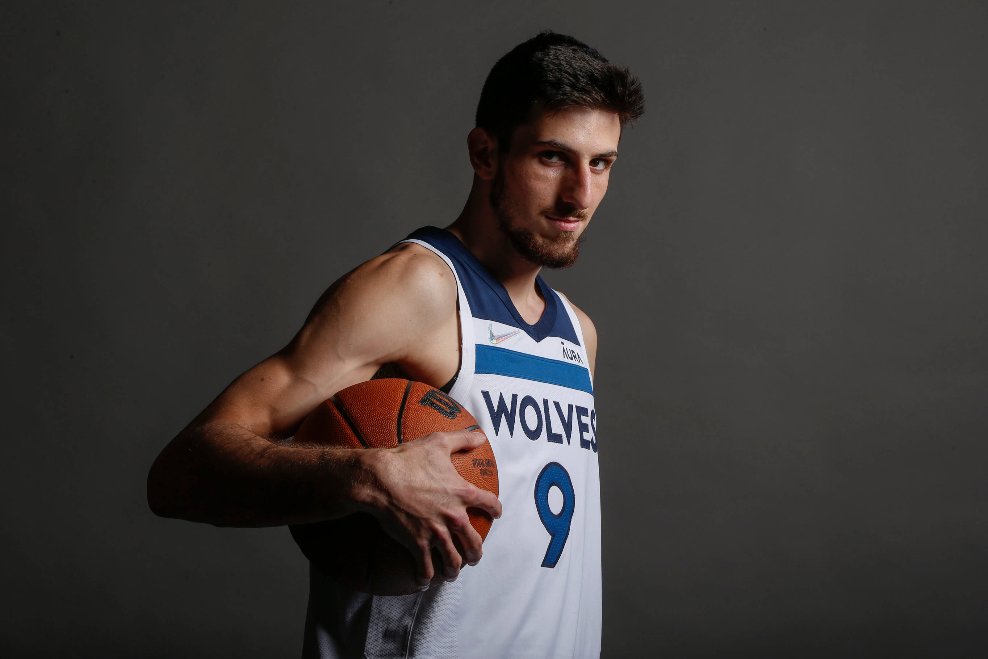 Timberwolves 桌布 壁紙 — 一名身穿狼隊球衣的籃球運動員在深灰色攝影棚背景前，在戲劇性燈光下持球。