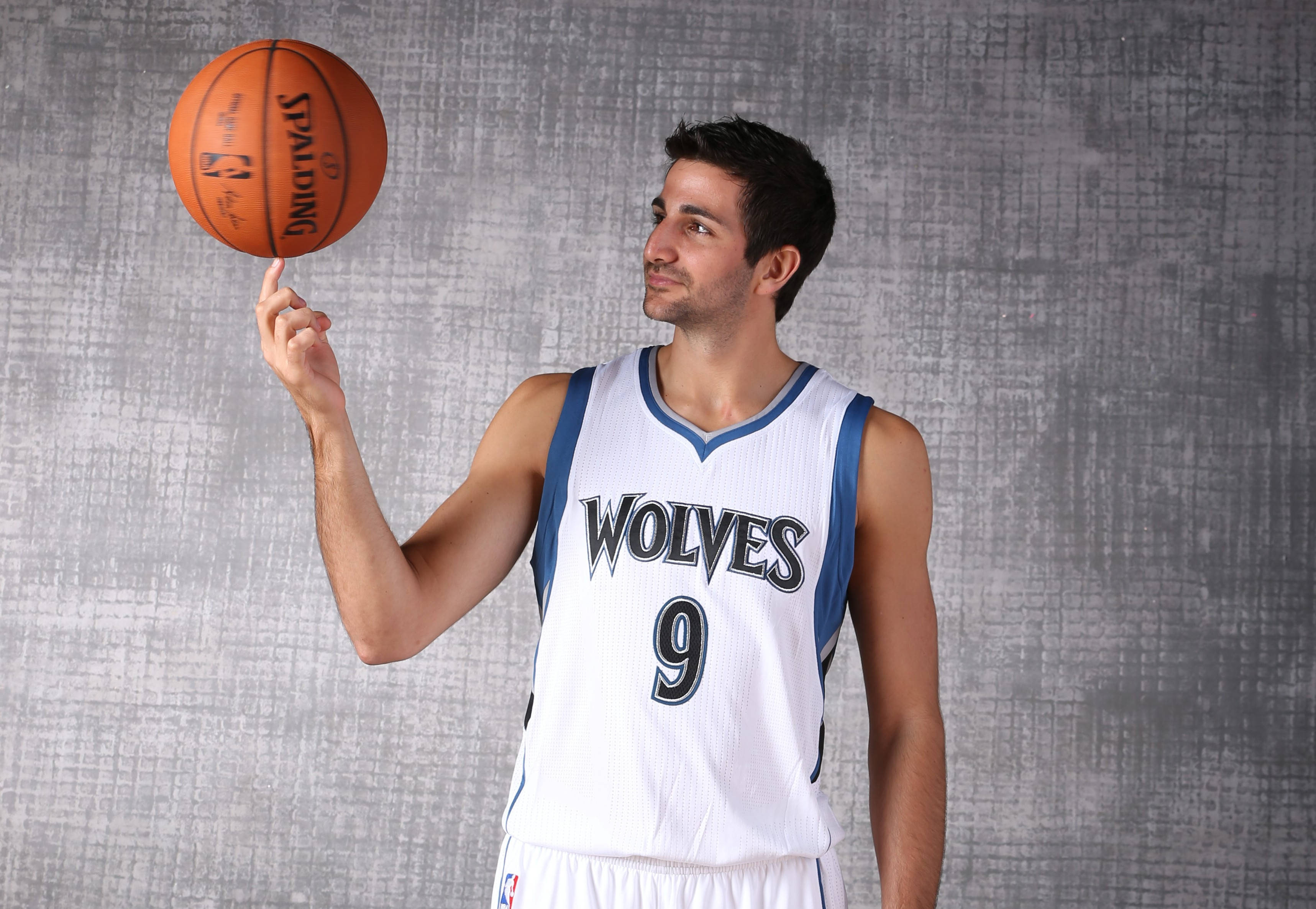 Ricky Rubio 桌布 壁紙 — 一名身穿狼隊球衣的籃球運動員在紋理灰色背景前，用指尖平衡一個橙色 Spalding 籃球。
