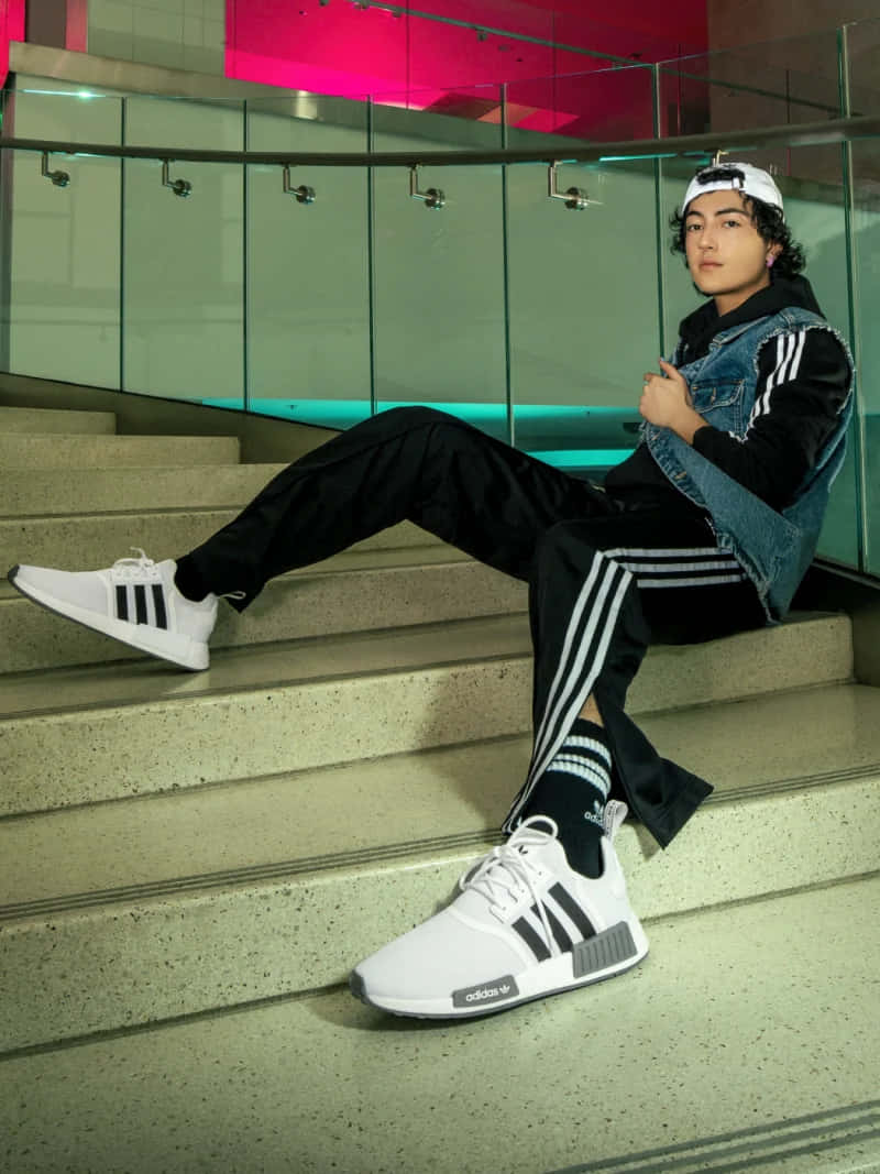 愛迪達 桌布 壁紙 — 一名身穿白色 adidas 運動鞋和牛仔背心的年輕男子，在霓虹粉紅和藍綠色燈光下，悠閒地躺在現代混凝土樓梯上。