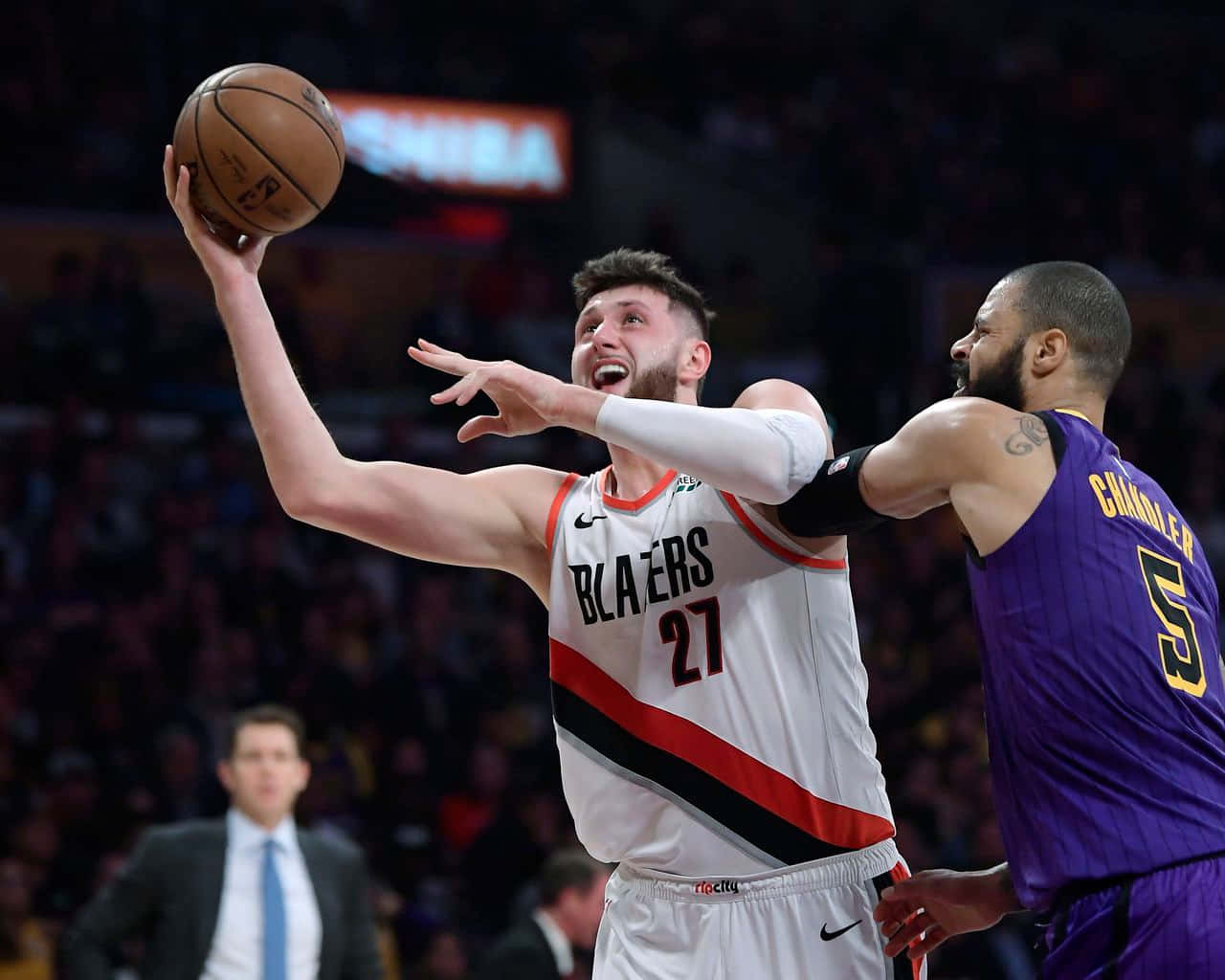籃球 桌布 壁紙 — 一名身穿白色 Blazers 球衣的籃球運動員在擠滿觀眾的場館內投籃，同時受到一名身穿紫色球衣的對手防守。