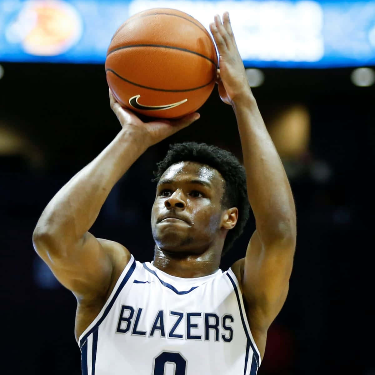 Bronny James 桌布 壁紙 — 一名身穿白色 Blazers 球衣的籃球運動員在場館燈光下準備投籃，神情專注。