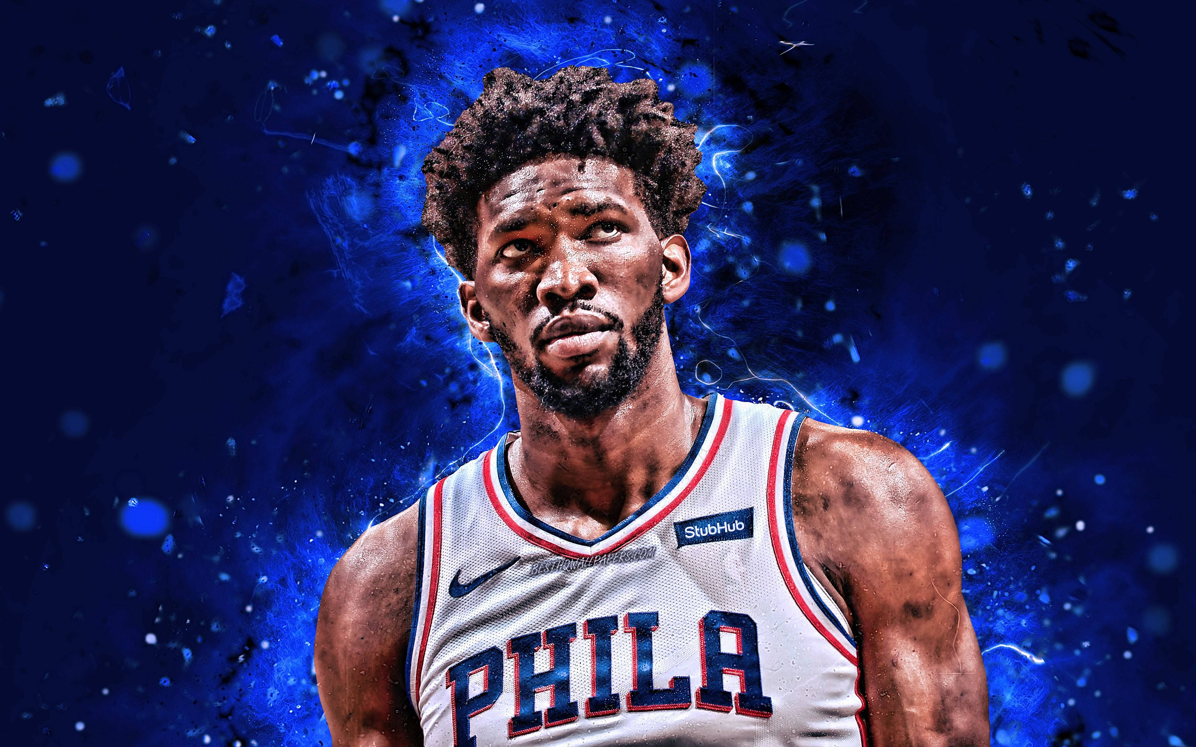 Embiid 桌布 壁紙 — 一名身穿白色「PHILA」球衣的籃球運動員，站在充滿活力的藍色宇宙背景前，帶有電能效果。
