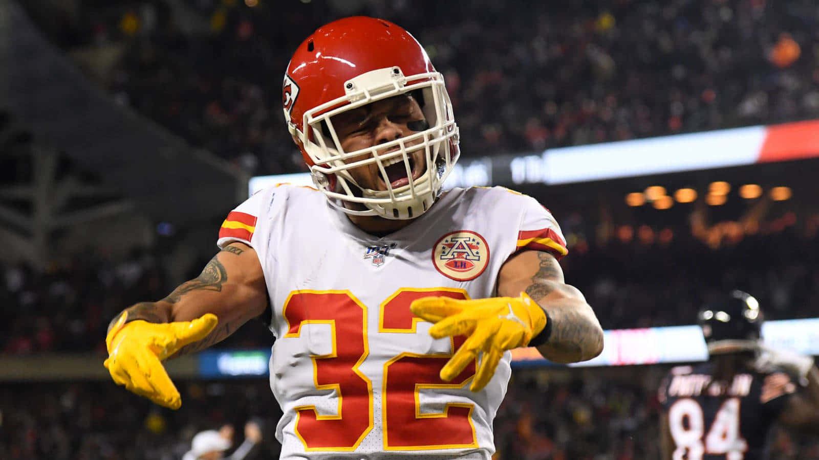 Tyrann Mathieu 桌布 壁紙 — 一名身穿白色、紅色和黃色球衣的堪薩斯城酋長隊美式足球員（32號）在球場燈光下熱情慶祝。