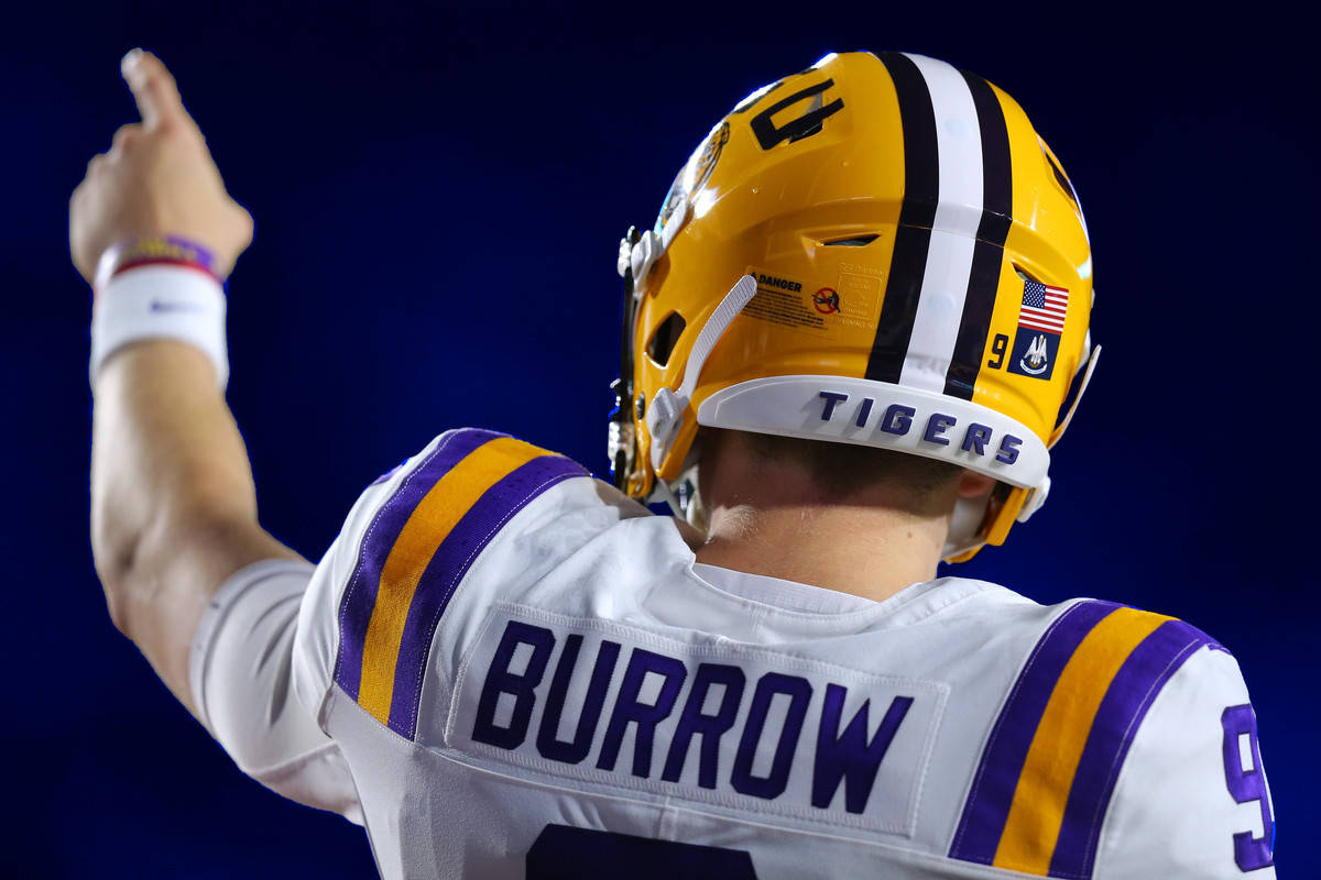 Joe Burrow 桌布 壁紙 — 一名身穿白色、紫色和金色球衣、背後印有「BURROW」的美式足球四分衛在球場燈光下豎起大拇指慶祝勝利。