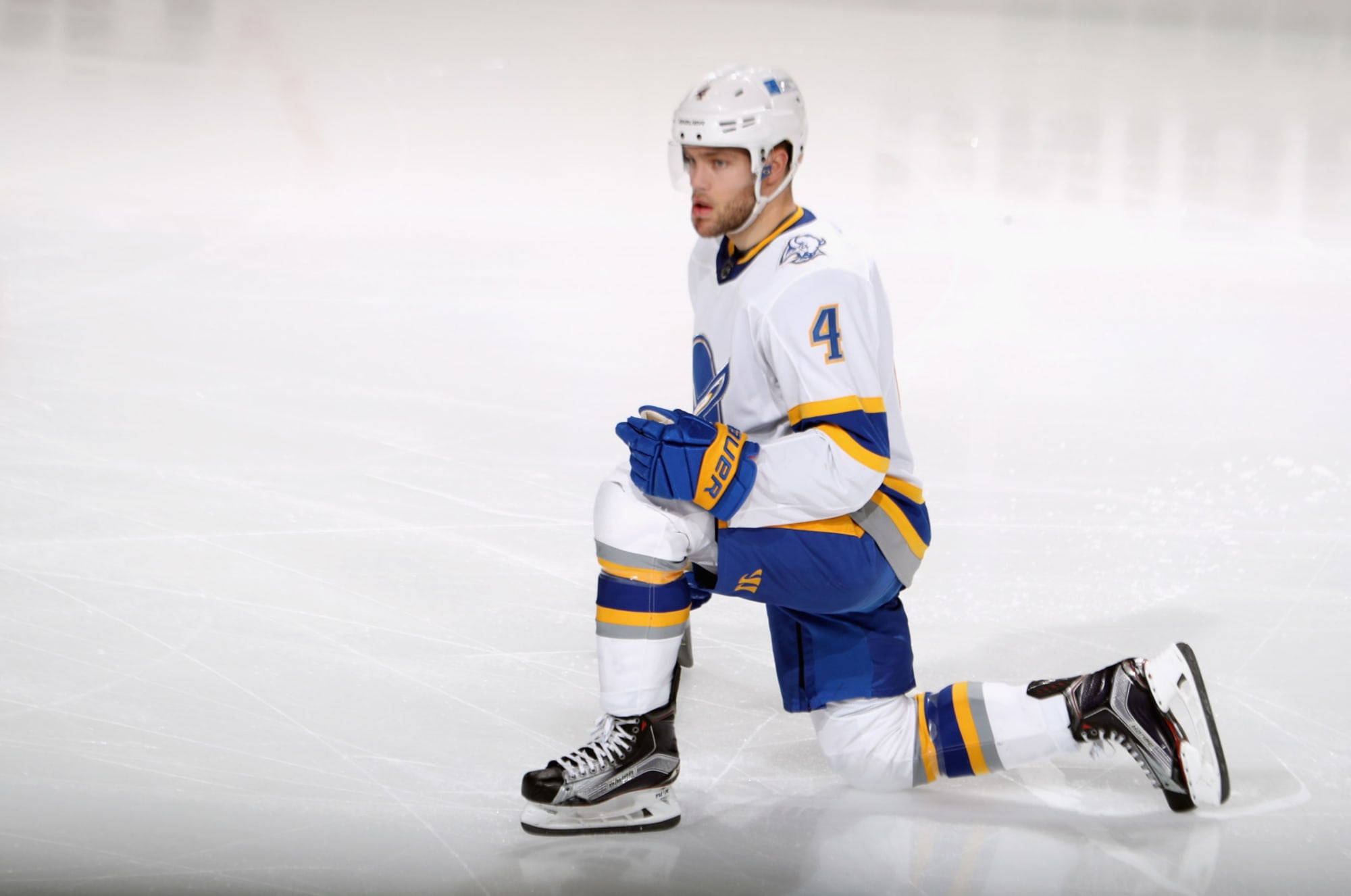 曲棍球 桌布 壁紙 — 一名身穿白色、藍色和金色球衣的冰球運動員在比賽期間跪在冰場上，神情專注。