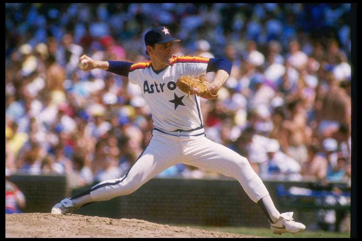 Nolan Ryan 桌布 壁紙 — 一名身穿白色Astros球衣的棒球投手在陽光明媚的投手丘上投球，背景是模糊的人群。