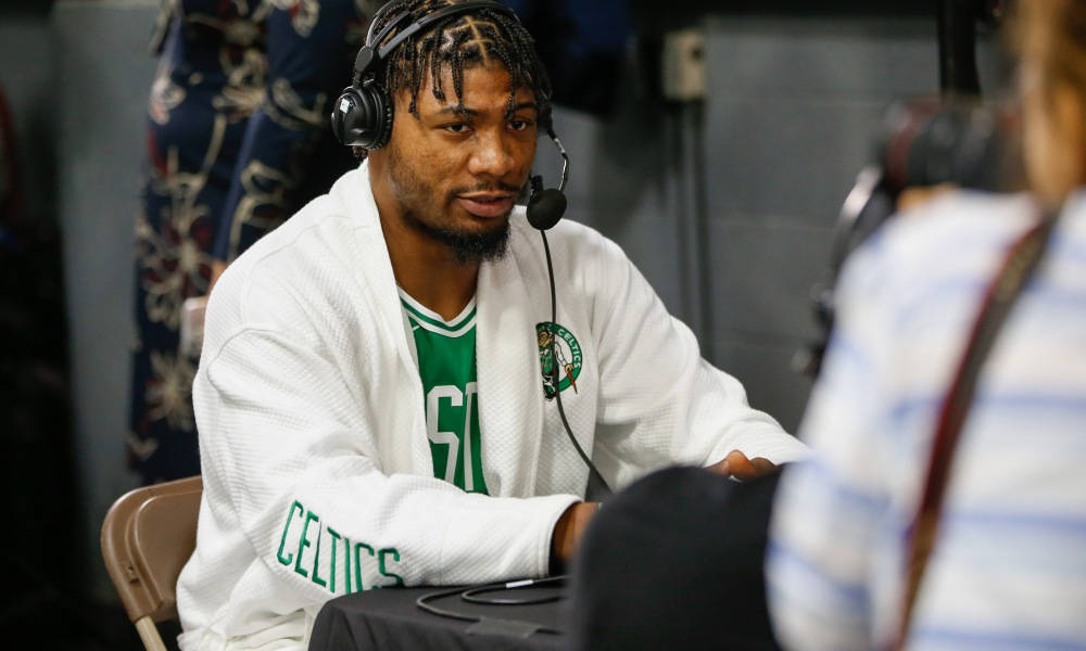 Marcus 桌布 壁紙 — 一名身穿白色Celtics連帽衫和耳機的籃球運動員在昏暗的房間裡專注地坐著接受媒體採訪。