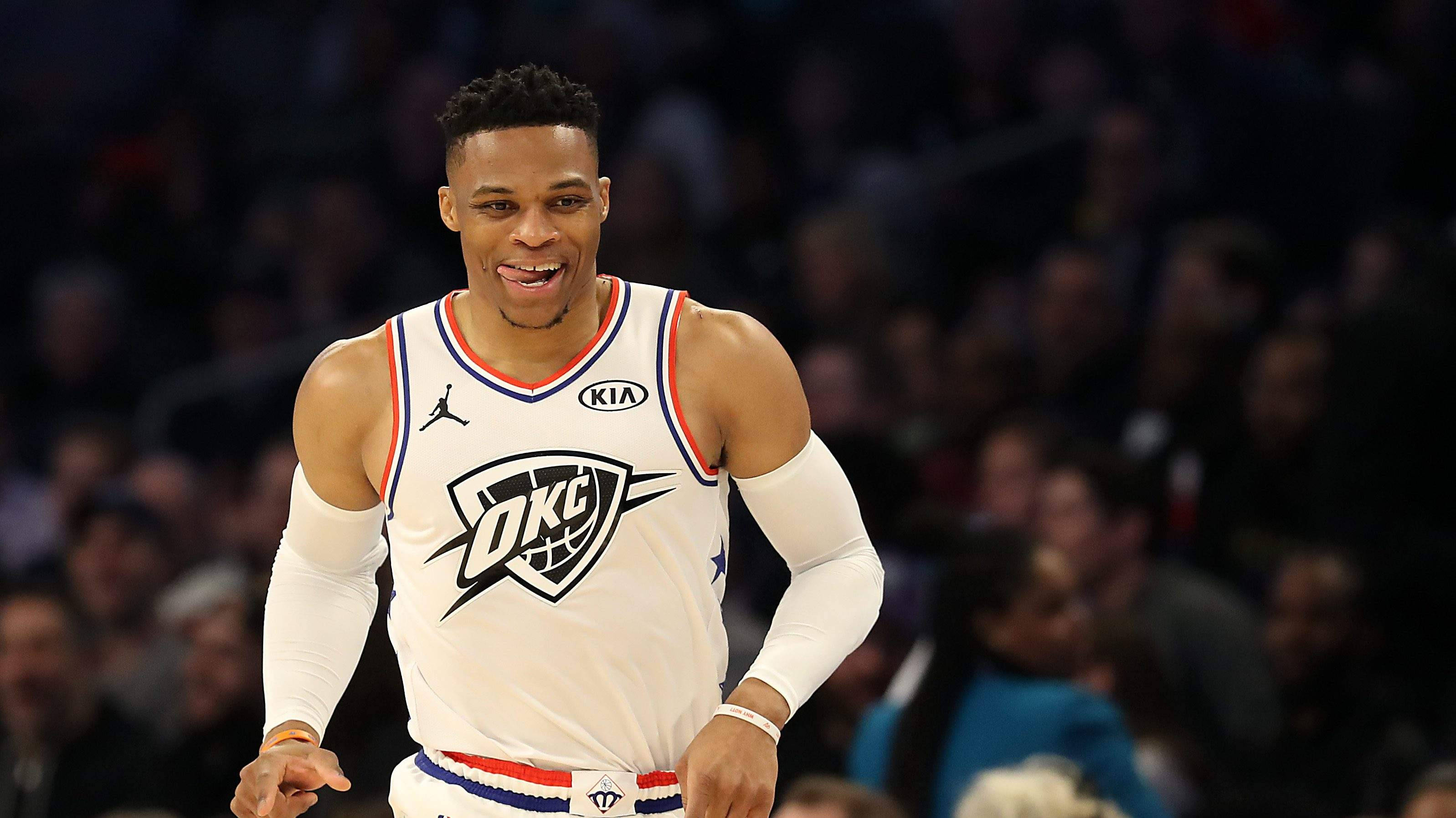 Westbrook 桌布 壁紙 — 一名身穿白色OKC球衣的籃球運動員在比賽中咧嘴大笑，身後是模糊的人群。