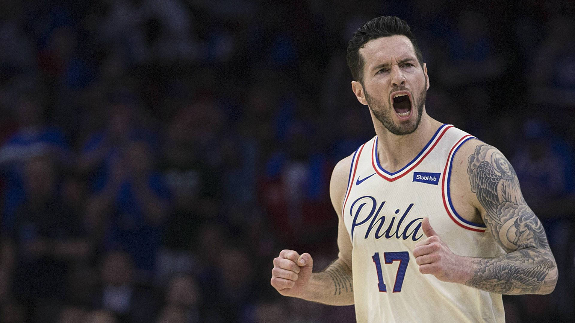 Jj Redick 桌布 壁紙 — 一名身穿白色Phila球衣的籃球運動員在場館燈光下比賽時握緊拳頭怒吼。