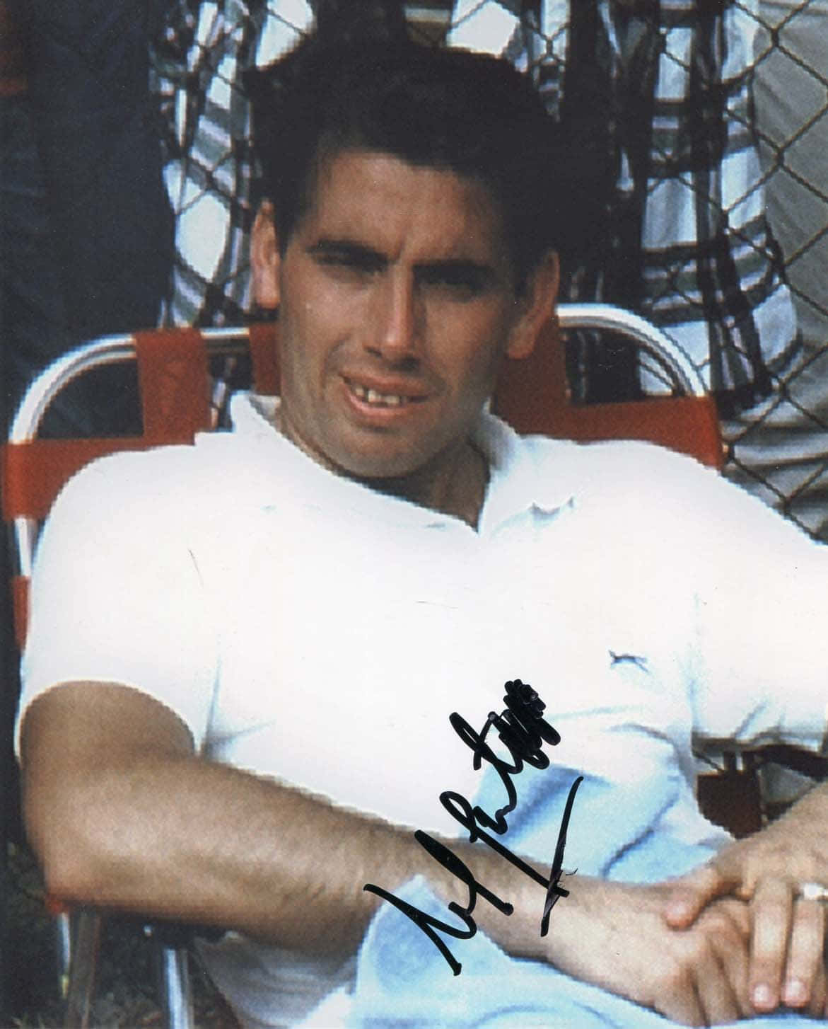 Tennis 桌布 壁紙 — 一名身穿白色Polo衫的男子坐在紅色椅子上，身後有鐵絲網圍欄，胸前有簽名，微微微笑。