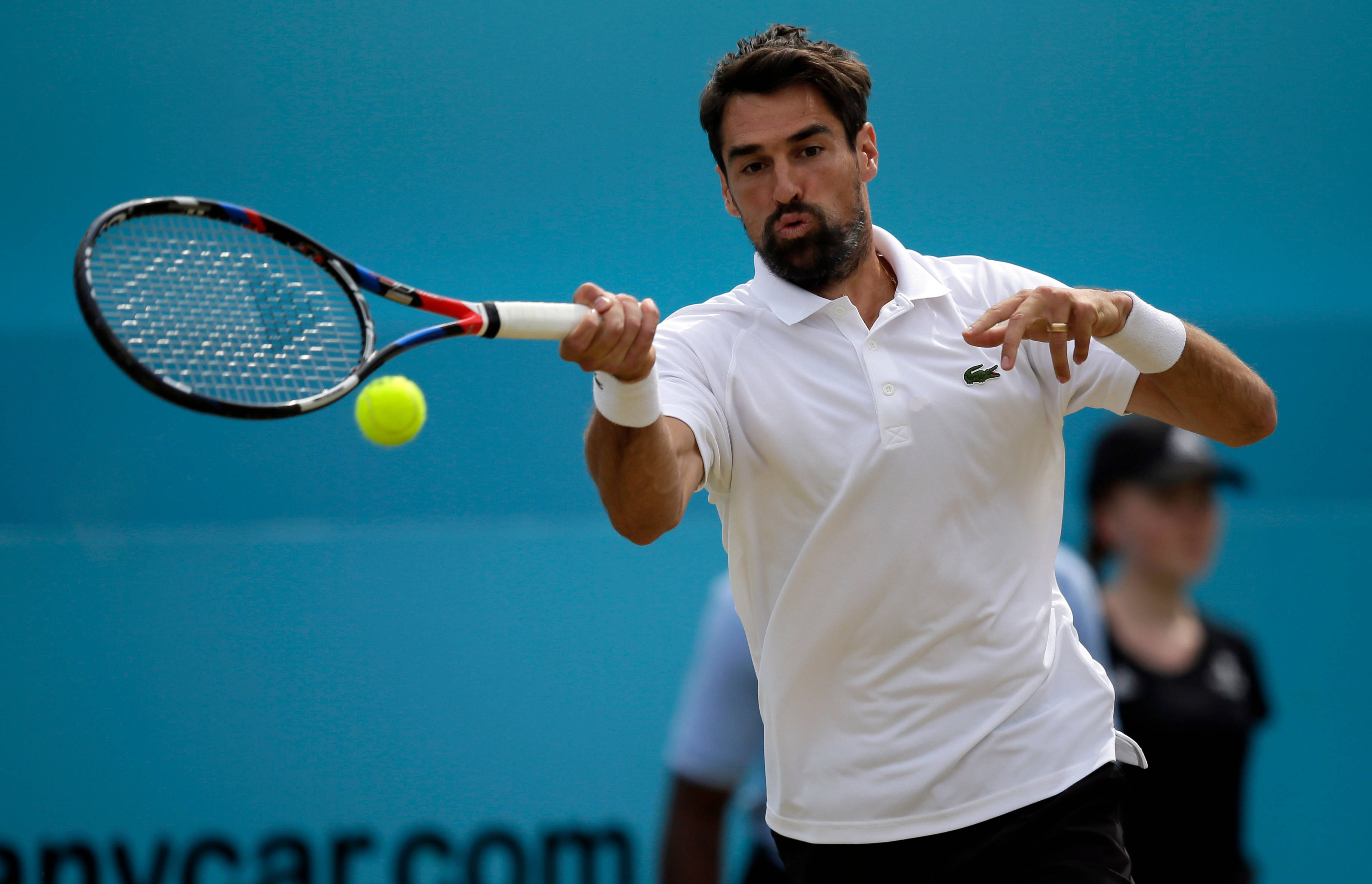 Tennis 桌布 壁紙 — 一名身穿白色Polo衫的男性網球選手揮動球拍，擊打一顆亮黃色的網球，背景為純藍色。