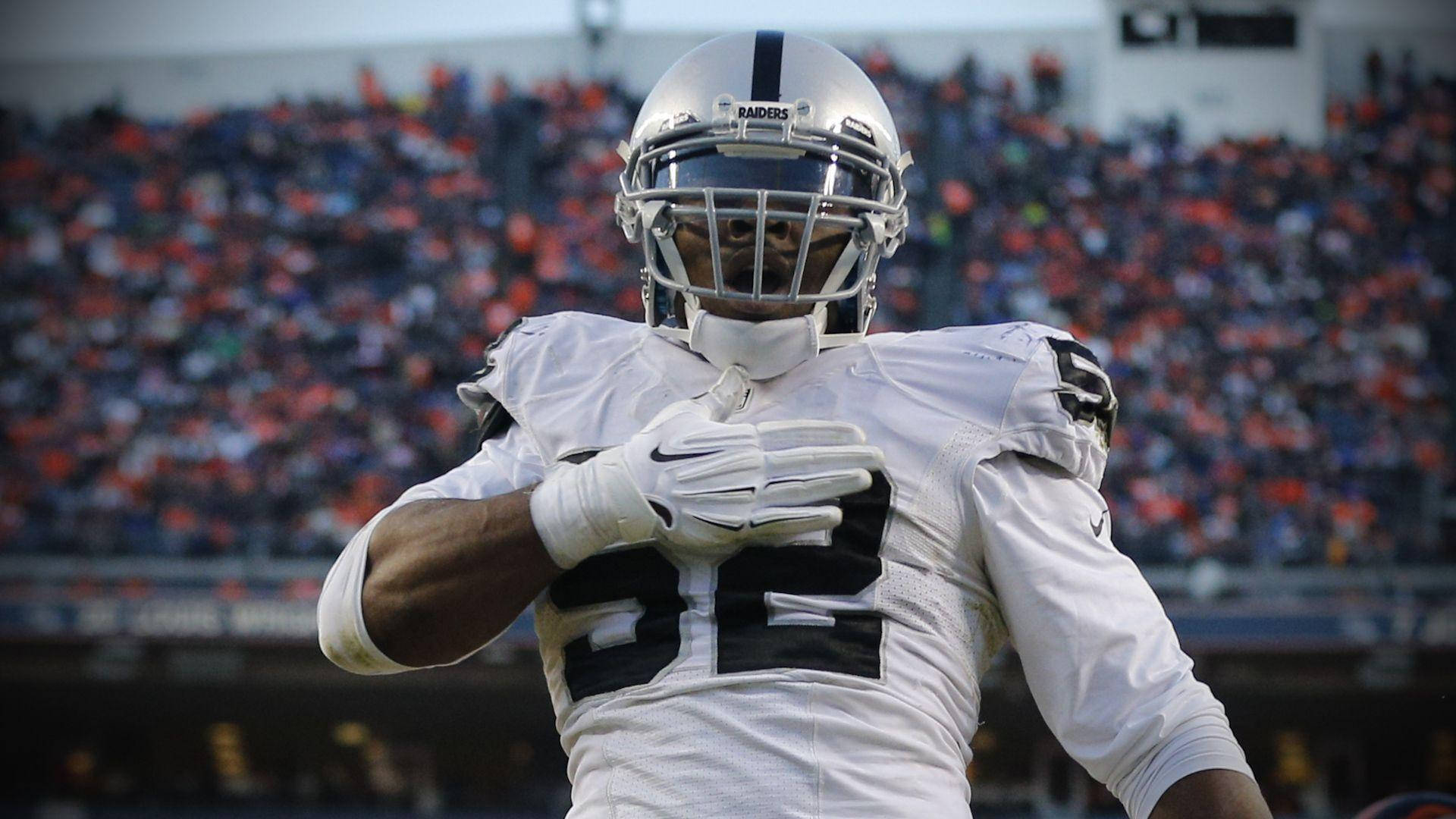 NFL 桌布 壁紙 — 一名身穿白色Raiders球衣、號碼22的美式足球選手在模糊的體育場人群前慶祝。
